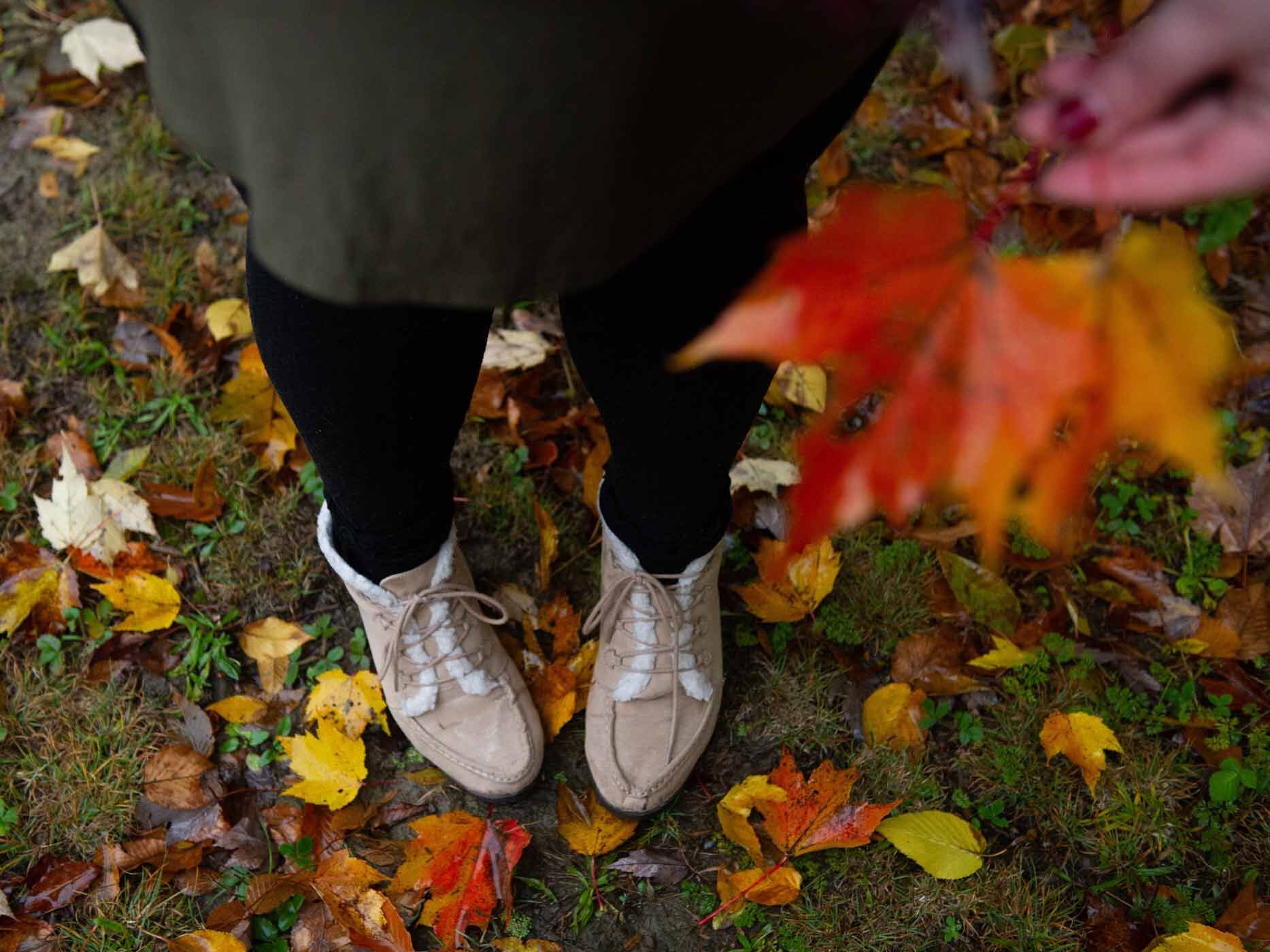 Frau steht im Herbstwald und trägt ein dunkelgrünes Blusenkleid mit einer schwarzen Leggings und braunen Stiefeln