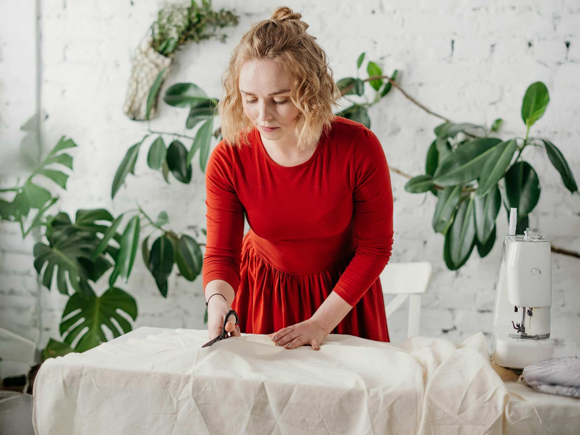 Eine Frau in einem roten Kleid steht vor einem weißen Kleid und schneidet es mit einer Schere.
