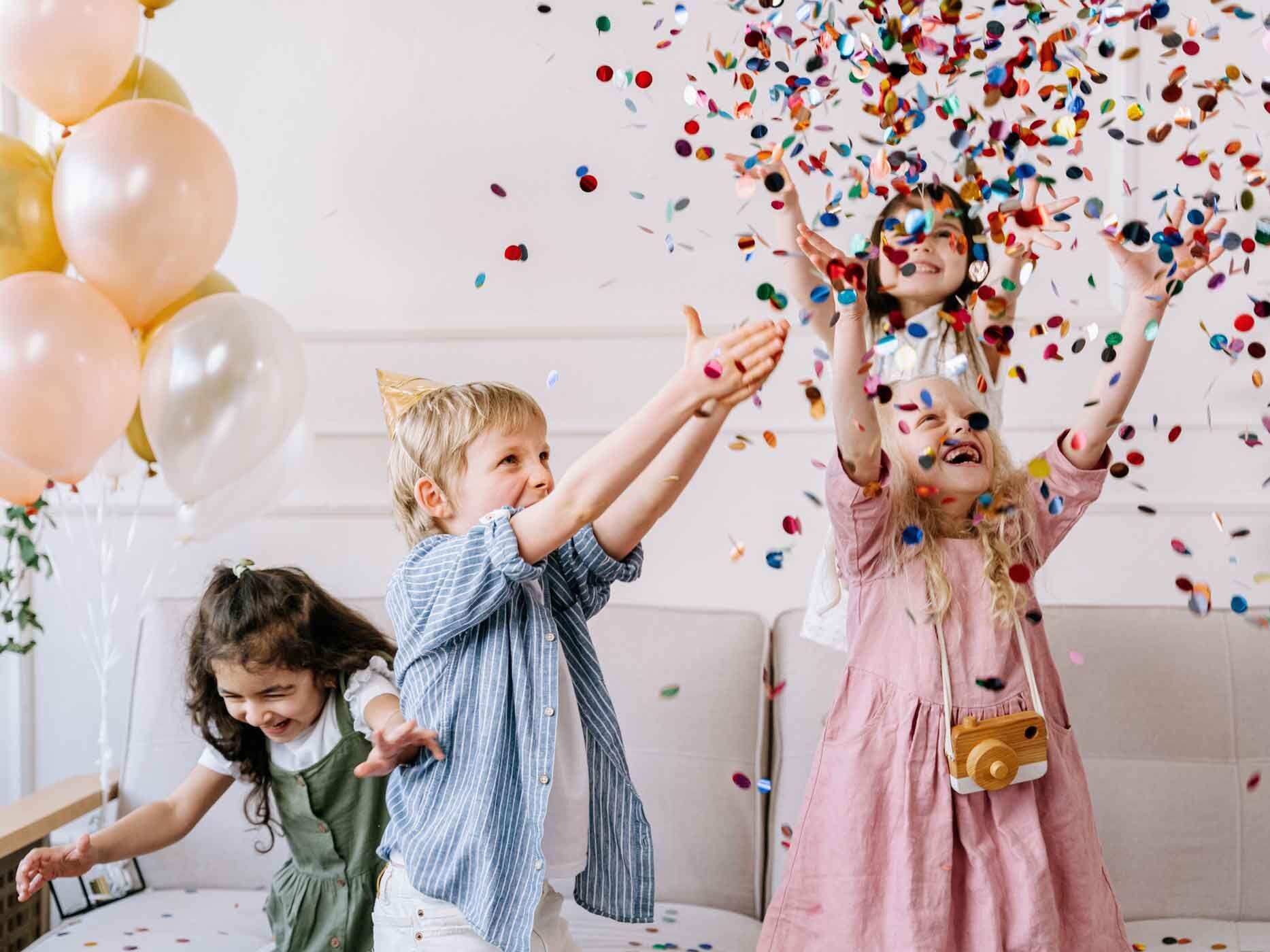 Kinder spielen mit Konfetti. Sie tragen Partyhüte und lachen.