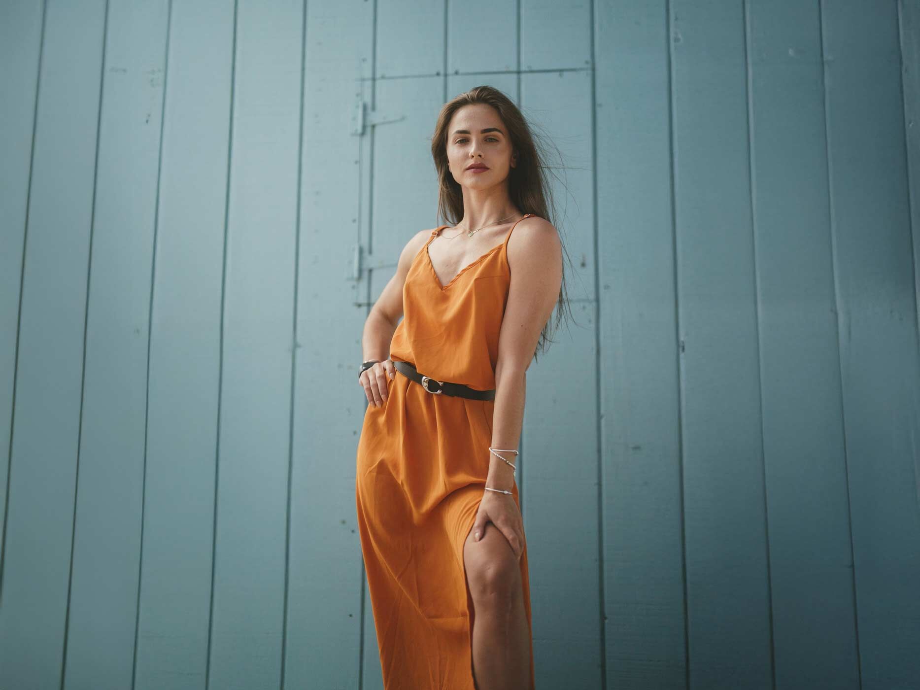 Eine Frau trägt ein oranges langes Sommerkleid und dazu einen schwarzen Gürtel um die Taillie. 