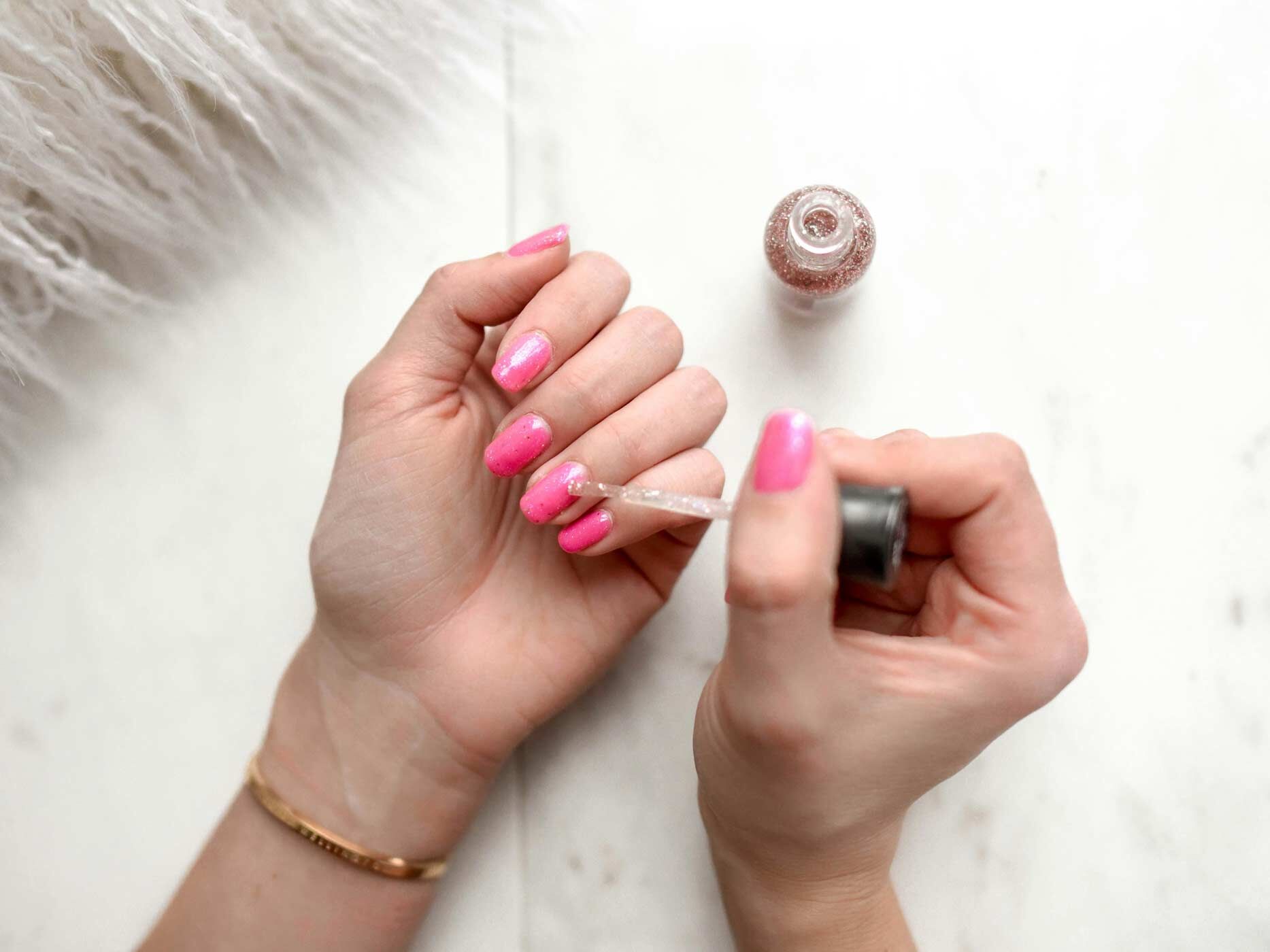 Eine Frau lackiert sich mit einer Hand die Fingernägel der anderen Hand in Neonpink.