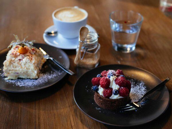 Ein Tisch im Café ist mit zwei Tellern mit Desserts, einer Tasse Kaffe und einem Glas Wasser gedeckt.