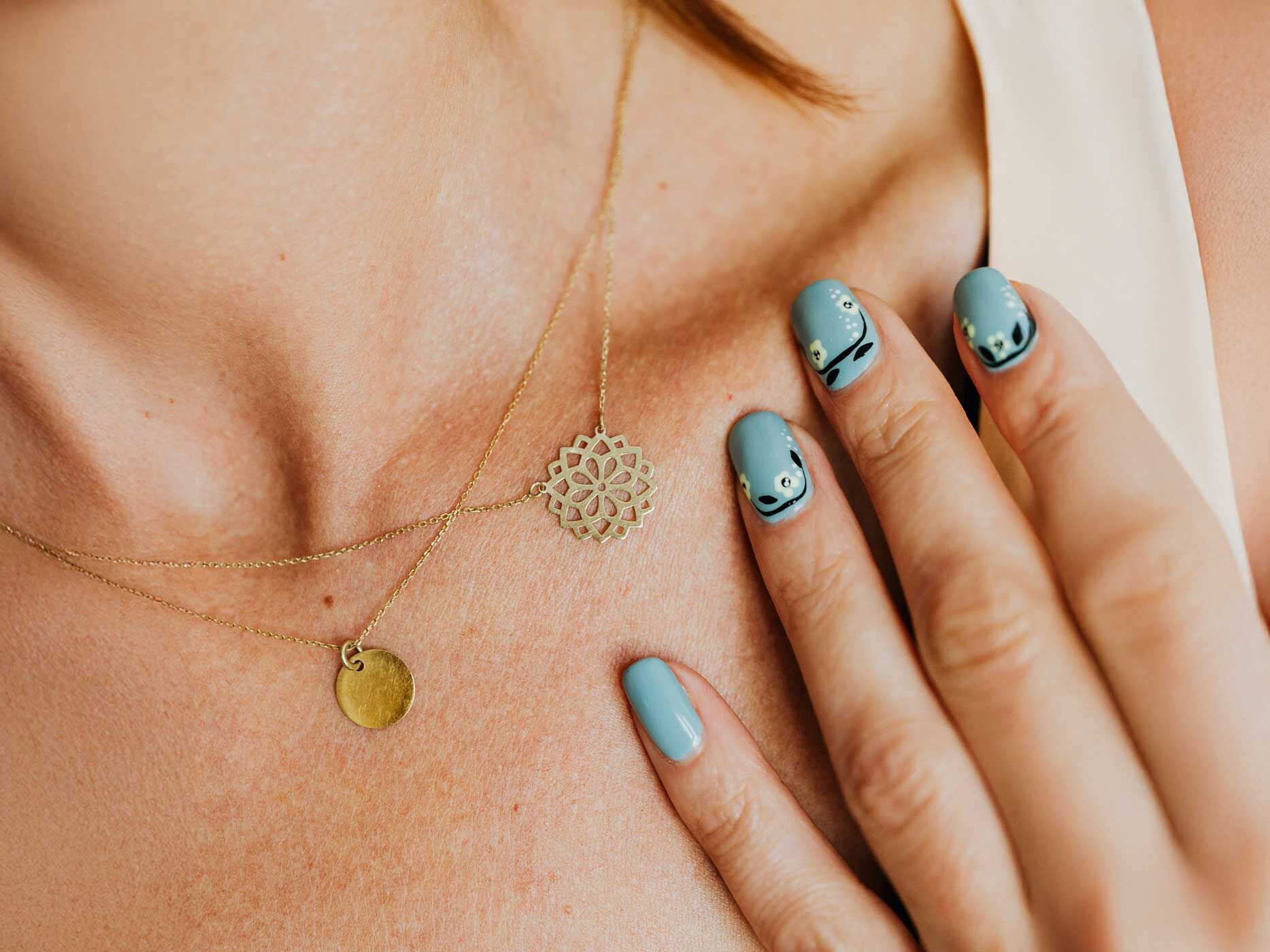 Eine Frau hält ihre Hand an ihren Hals, ihre Fingernägel sind blau lackiert und haben florale Muster darauf.