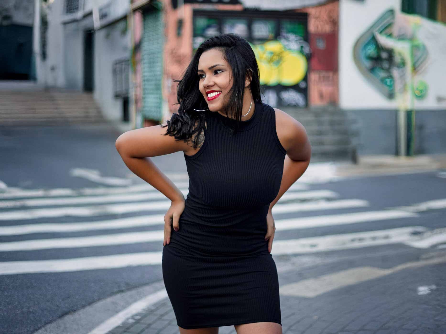 Eine Frau steht auf der Straße und posiert in einem eng anliegendem, schwarzen Kleid.