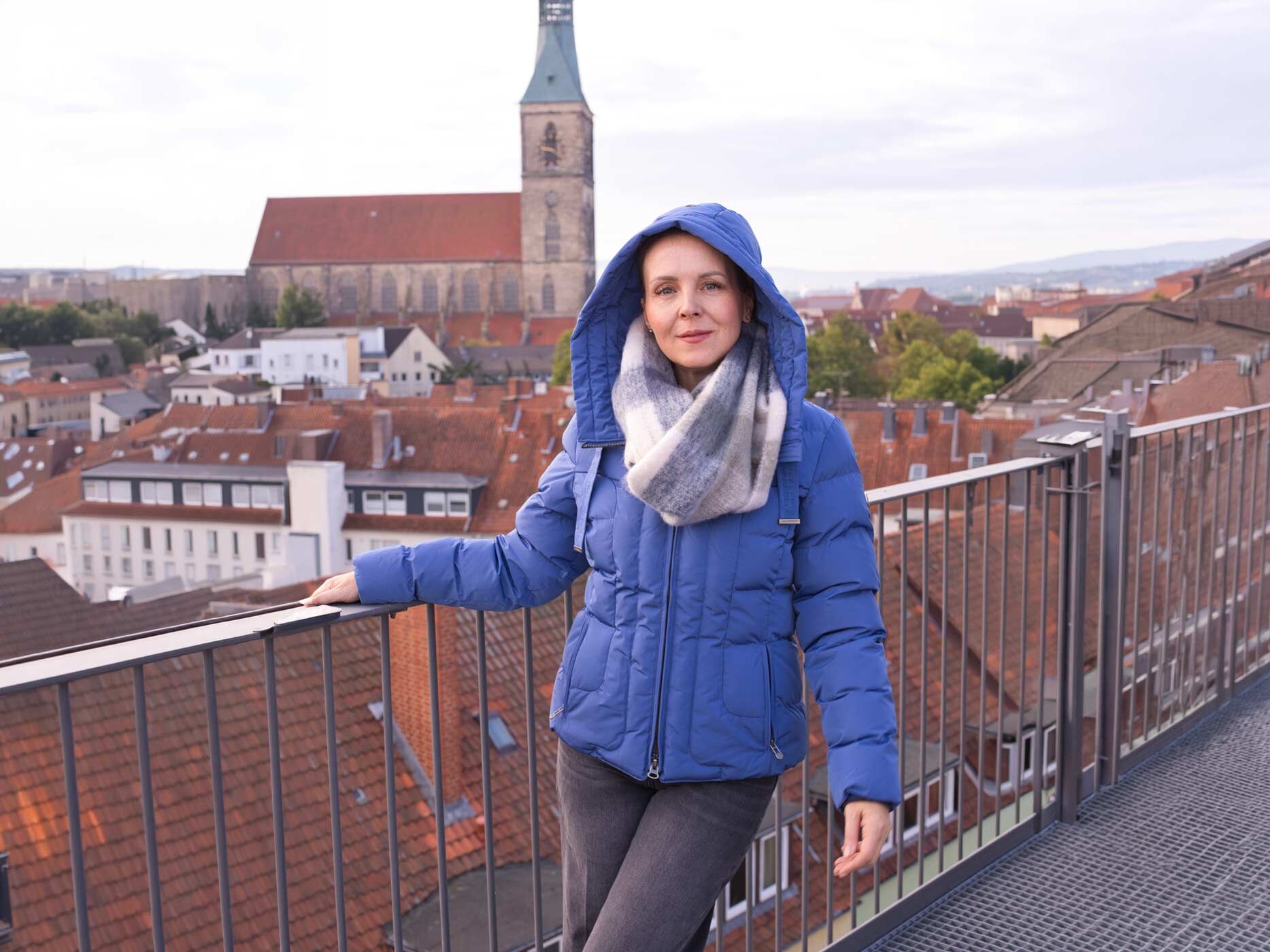 Eine Frau steht an einem Gel&auml;nder, sie tr&auml;gt eine graue Jeans und dazu eine lila Jacke.