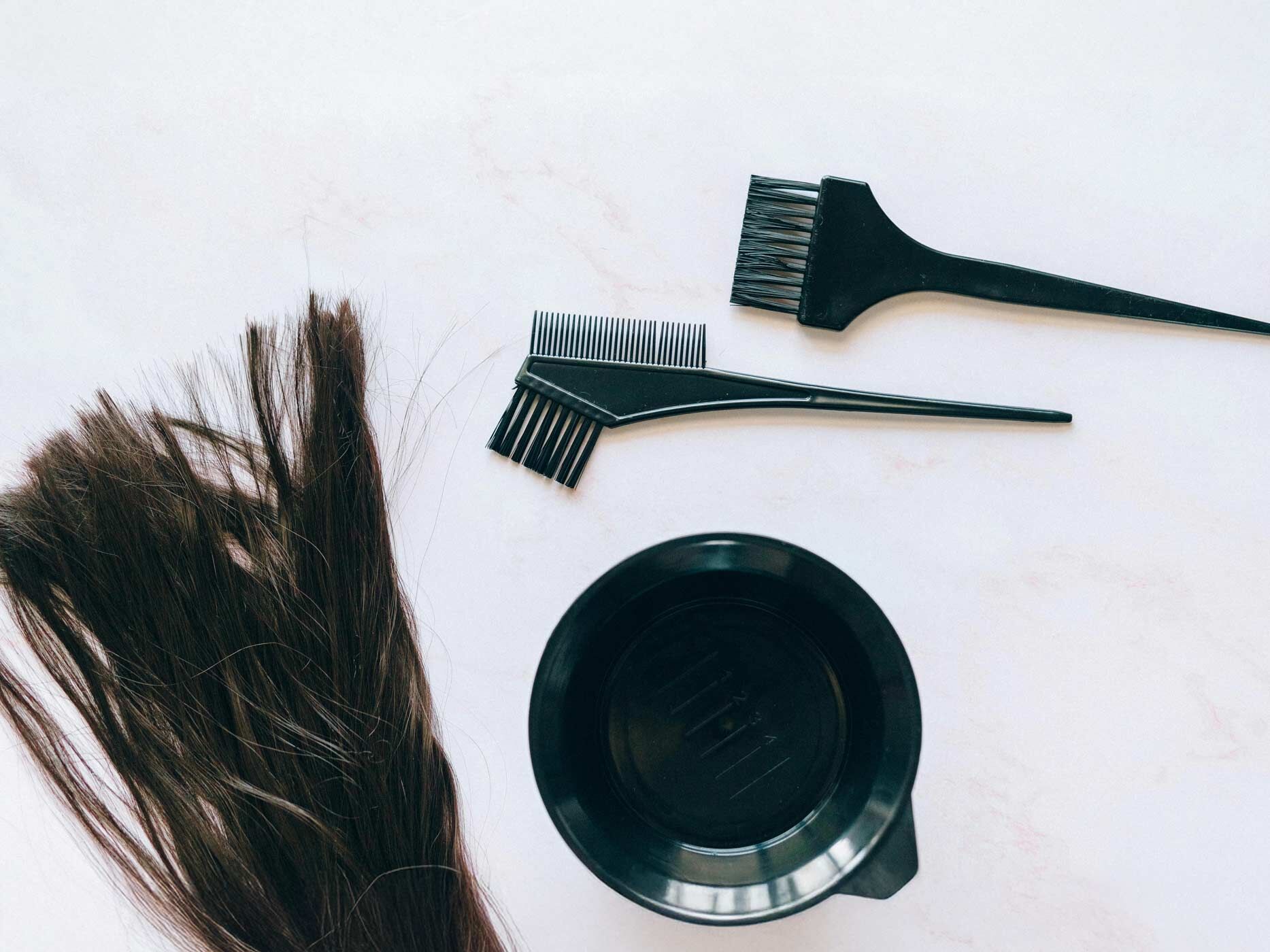 Eine braune Haarsträhne liegt neben Färbeutensilien