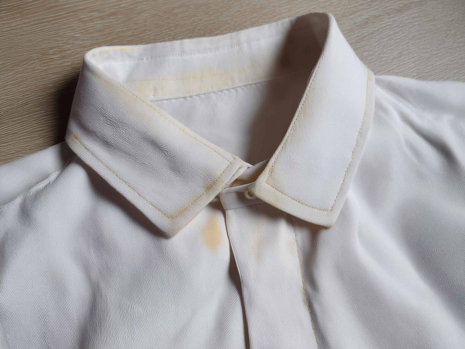 Ein weißes Poloshirt hat gelbe Verfärbungen am Kragen.