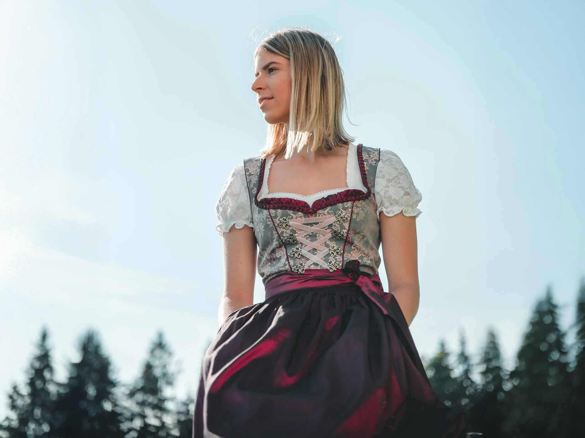 Eine Frau trägt ein dunkelrotes Dirndl, ihre Schleife ist auf der linken Seite gebunden.