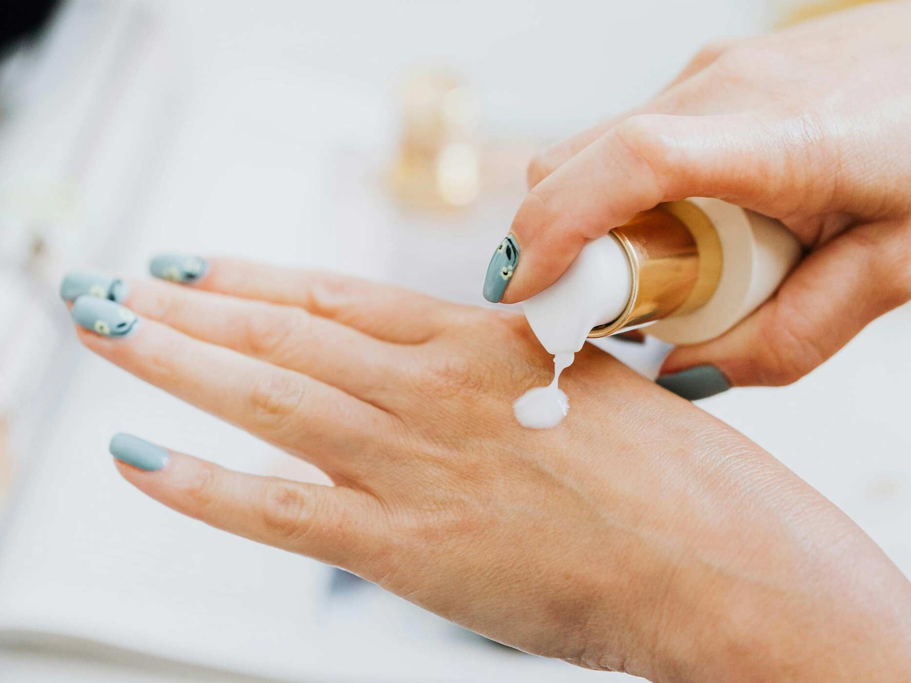 Eine Frau gibt sich etwas Creme auf den Handrücken. Die Nägel sind aufwendig lackiert.