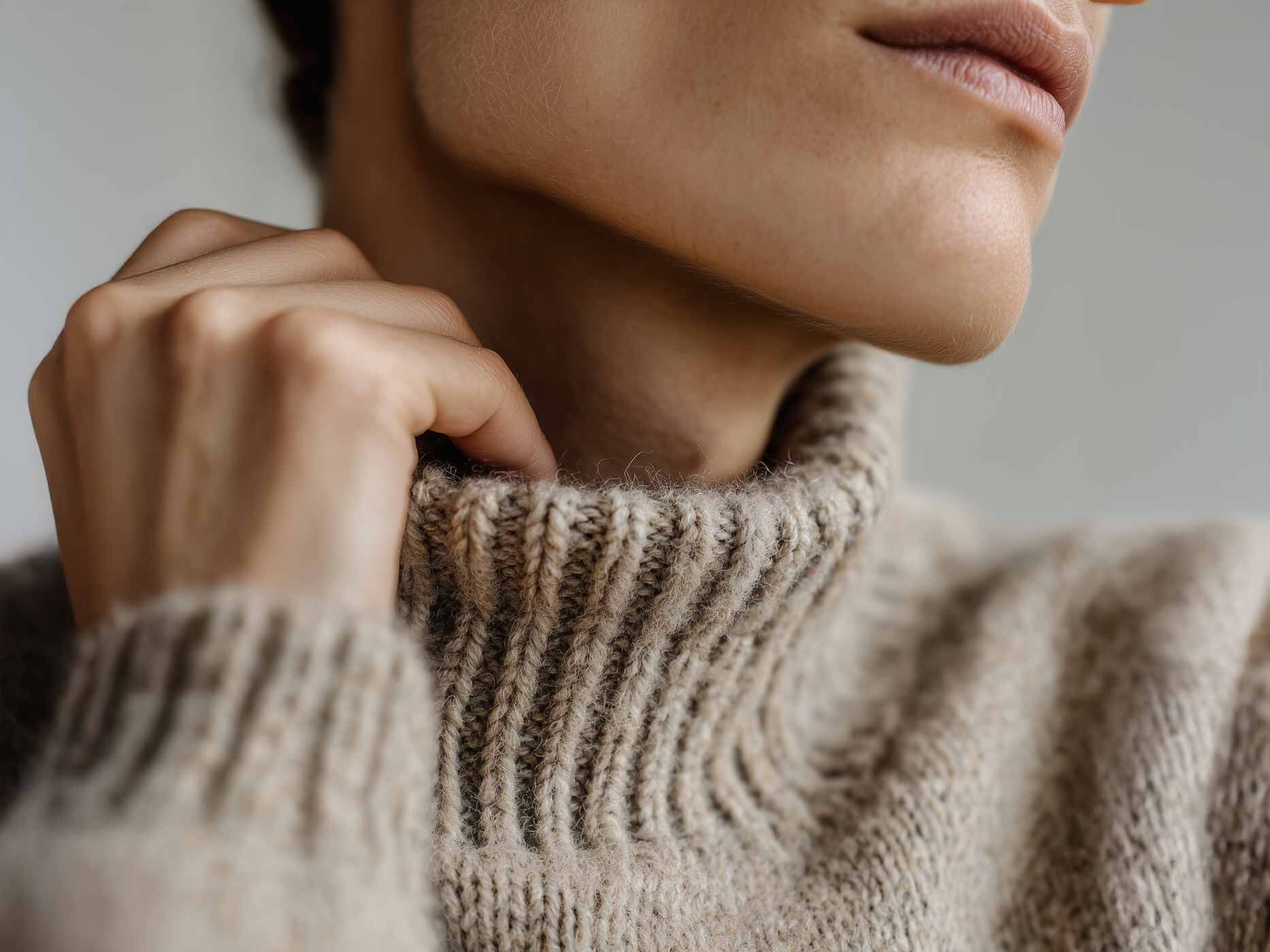 Nahaufnahme vom Hals einer Frau, der mit einem Rollkragenpullover aus Wolle bedeckt ist, ihre Hand kratzt am Hals unter dem Pullover.