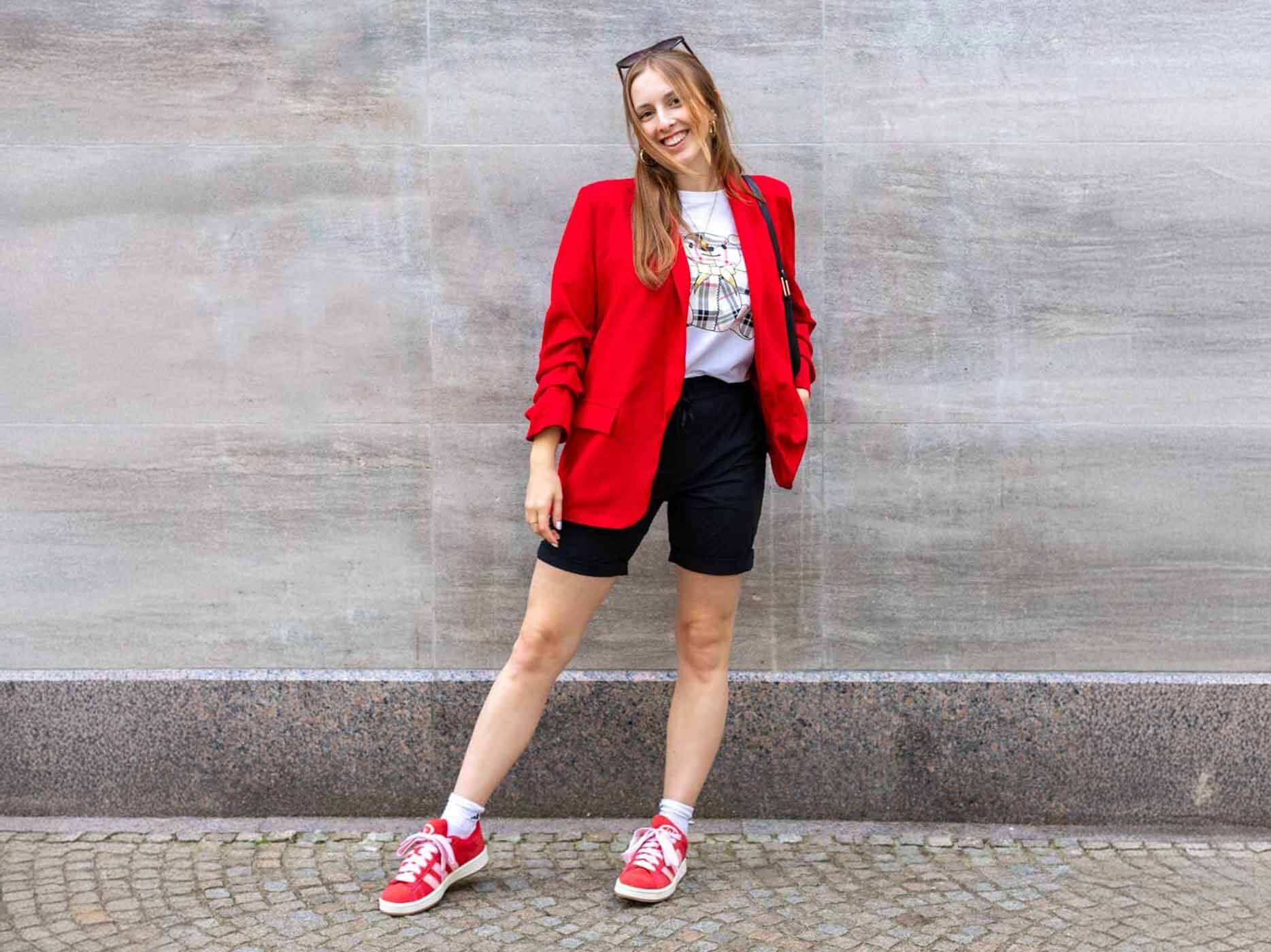 Ein junges Mädchen trägt eine kurze, schwarze Stoffhose, ein weißes T-Shirt und dazu einen roten Blazer.