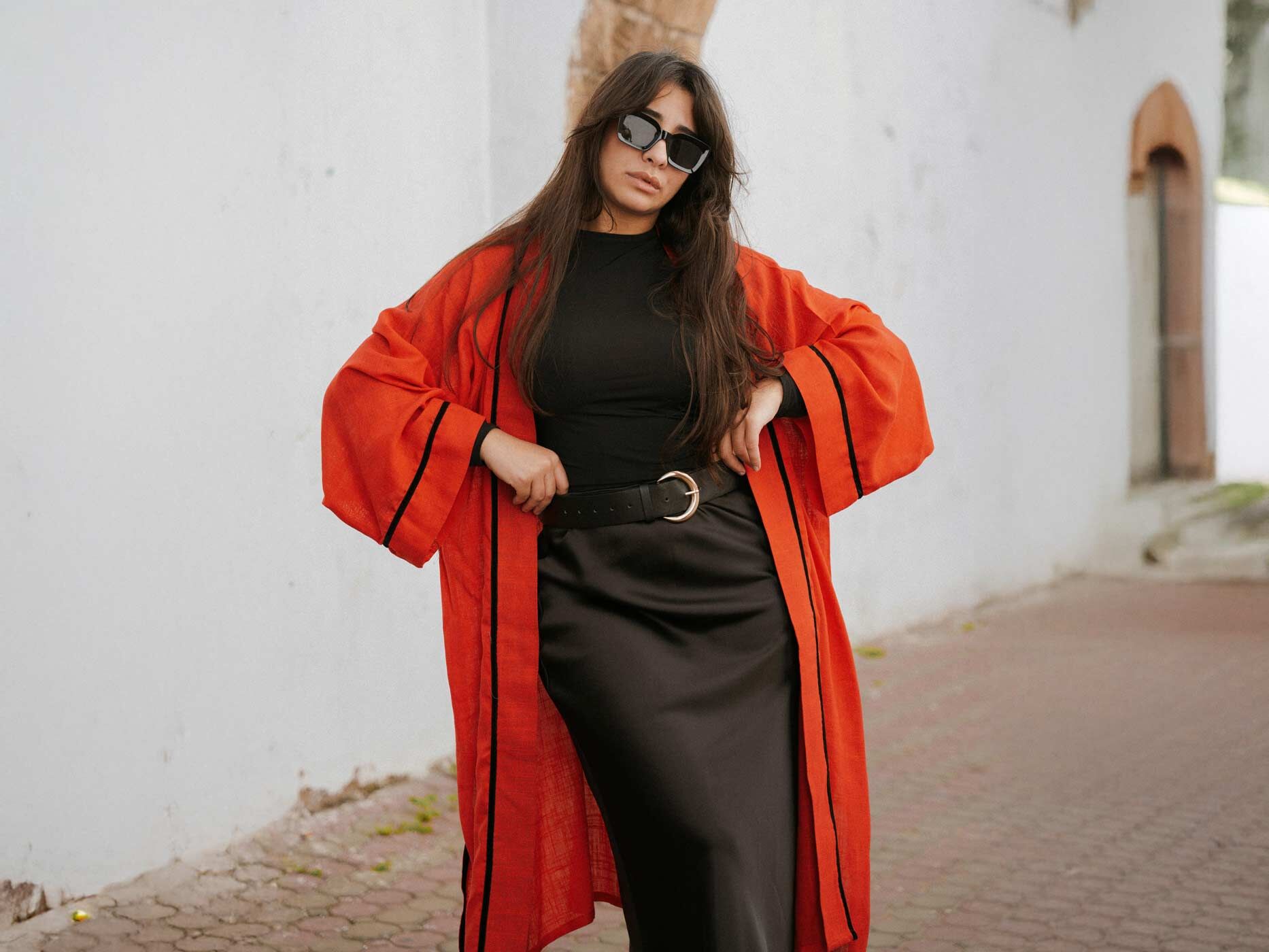 Eine Frau trägt ein schwarzes Kleid und dazu einen großen, auffälligen schwarzen Gürtel und einen roten Mantel.