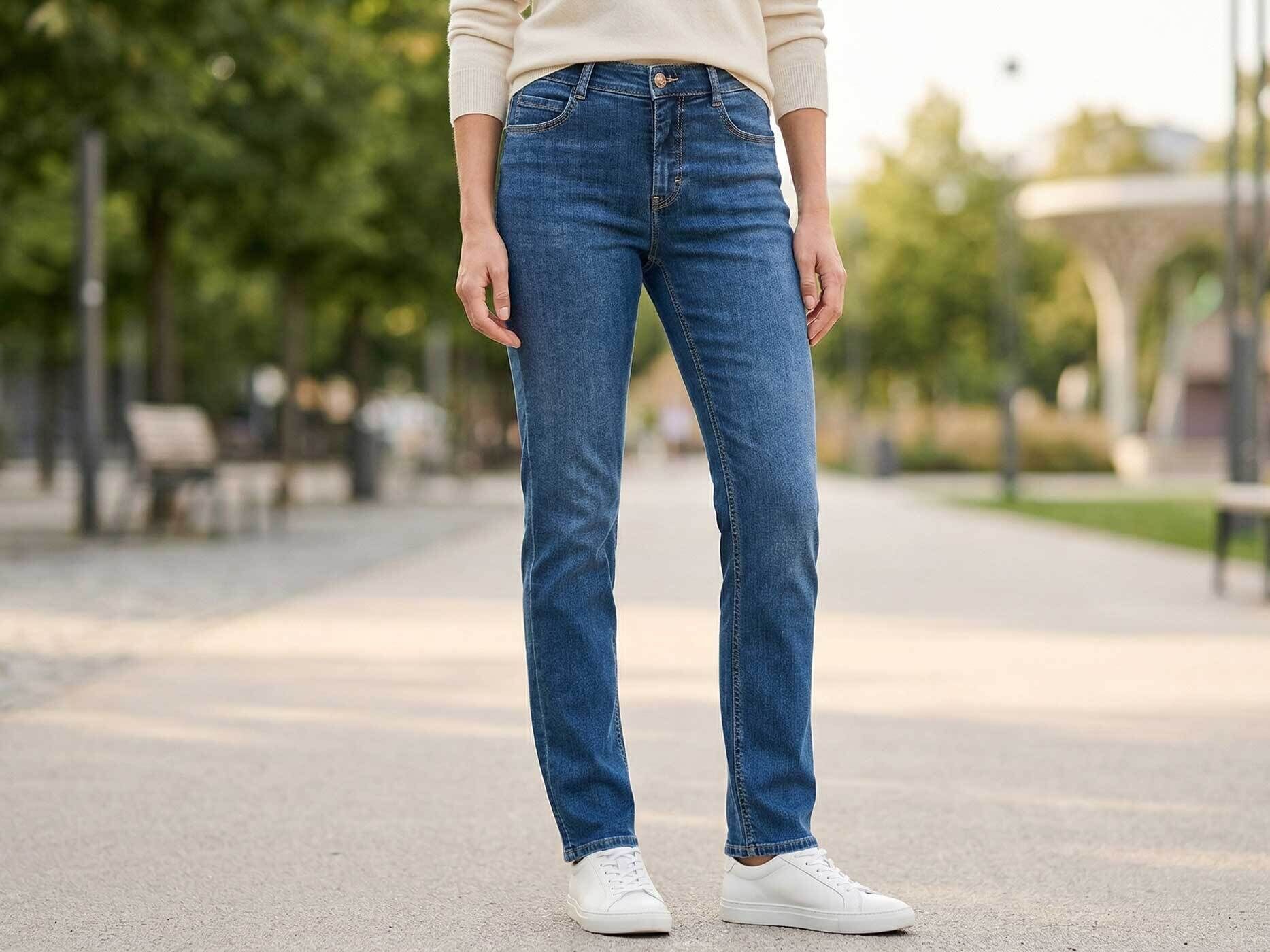 Eine Frau steht auf einem Weg. Nur ihr Unterkörper ist zu sehen. Sie trägt eine blaue Jeans mit weißen Sneakern.