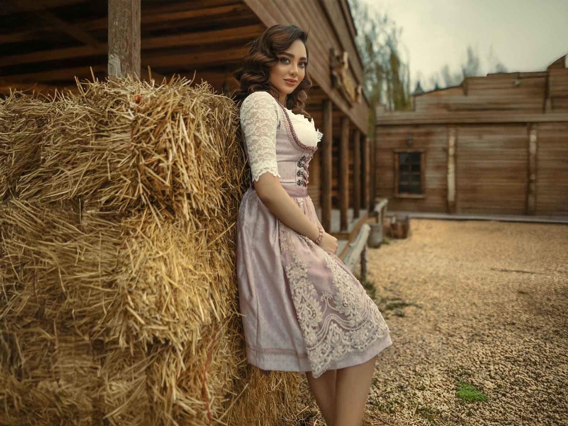 Eine Frau in einem rosafarbenen Dirndl lehnt gegen einen Strohballen.