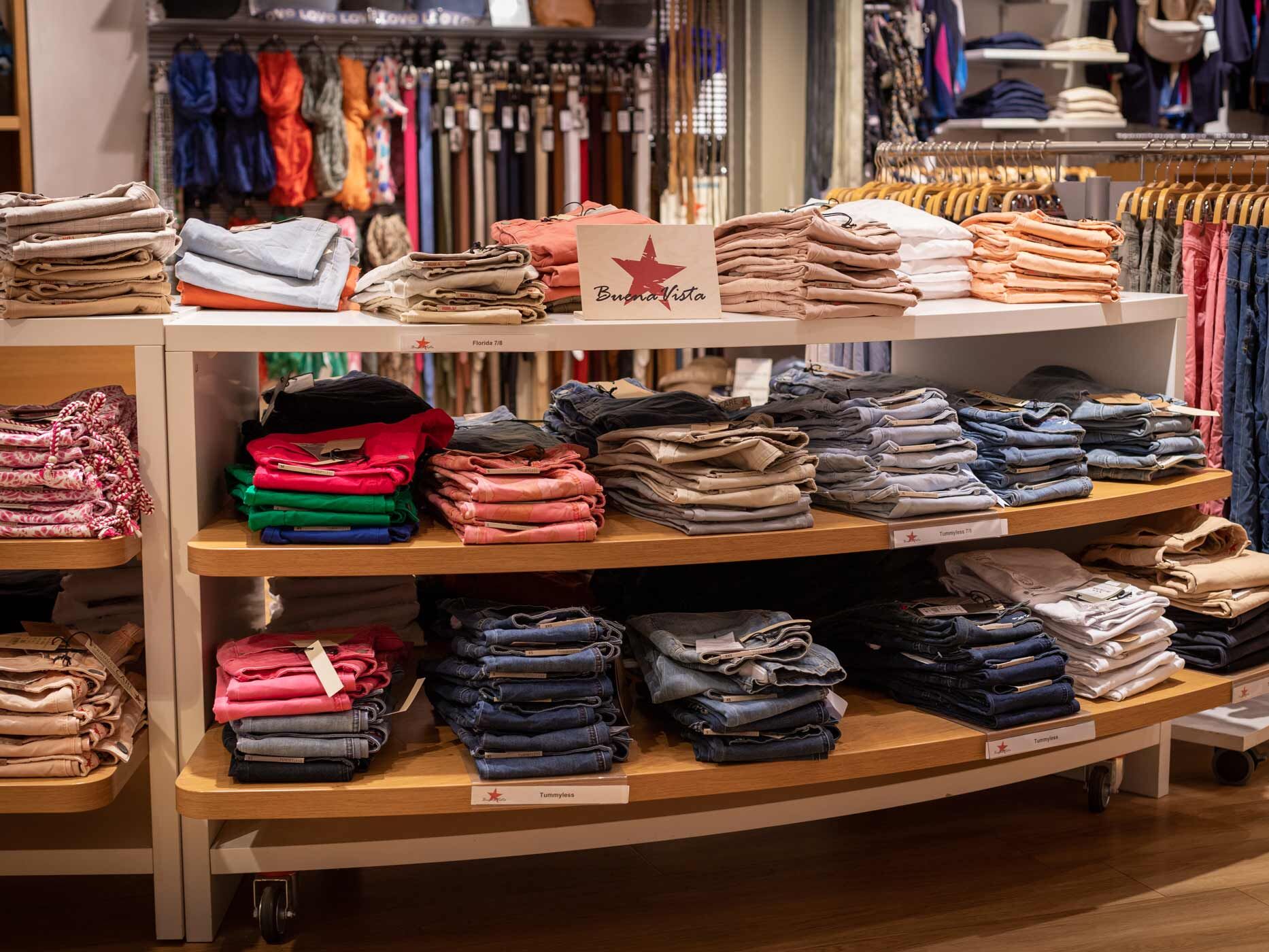 Verkaufsfl&auml;che mit einer gro&szlig;en Auswahl an Buena Vista Damenjeans in verschiedenen Farben und Waschungen. Die Hosen sind ordentlich gefaltet und nach Modellen auf mehreren Ebenen sortiert.