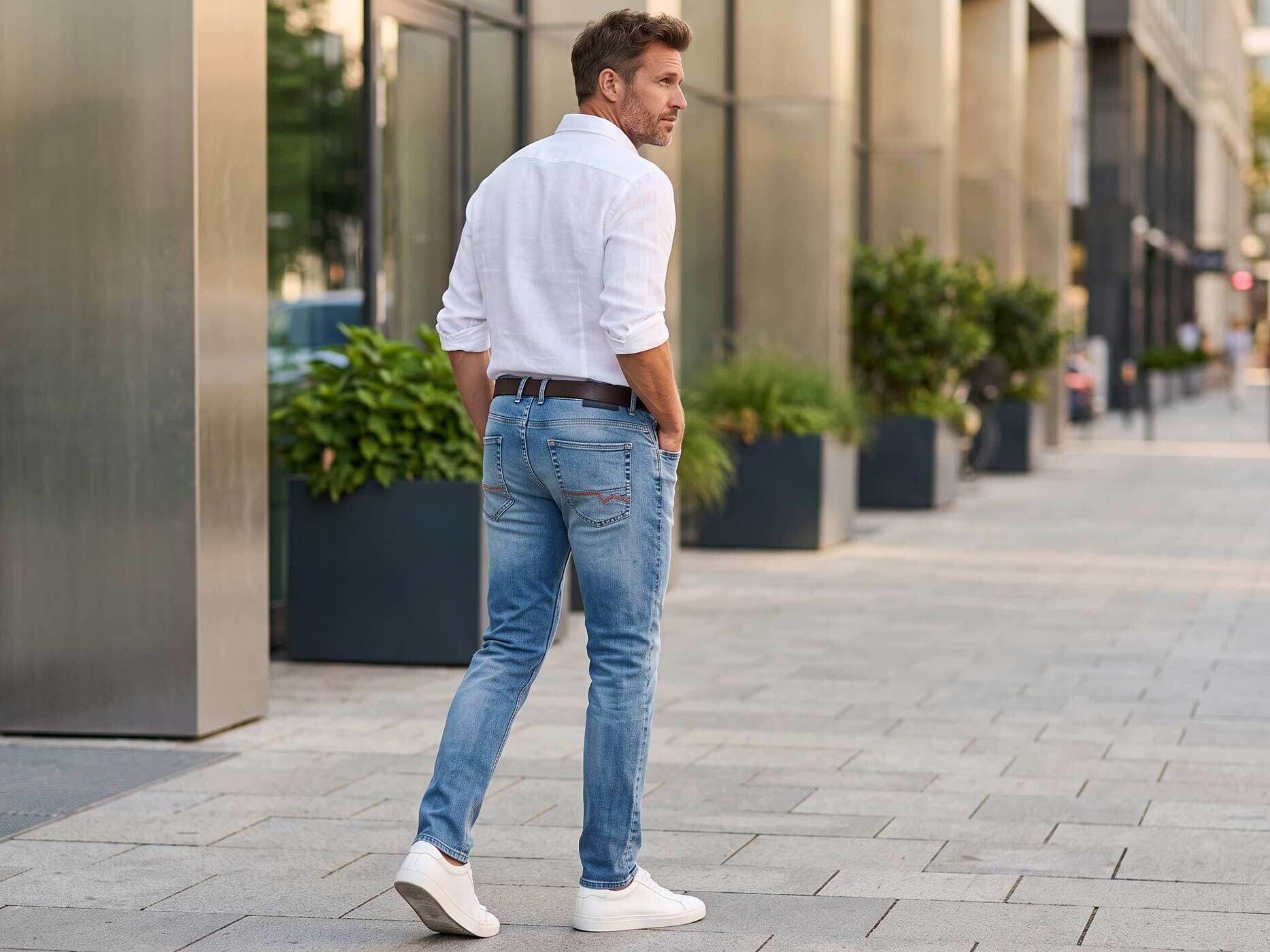 Ein Mann trägt eine hellblaue Jeans mit weißem Hemd und weißen Sneakern