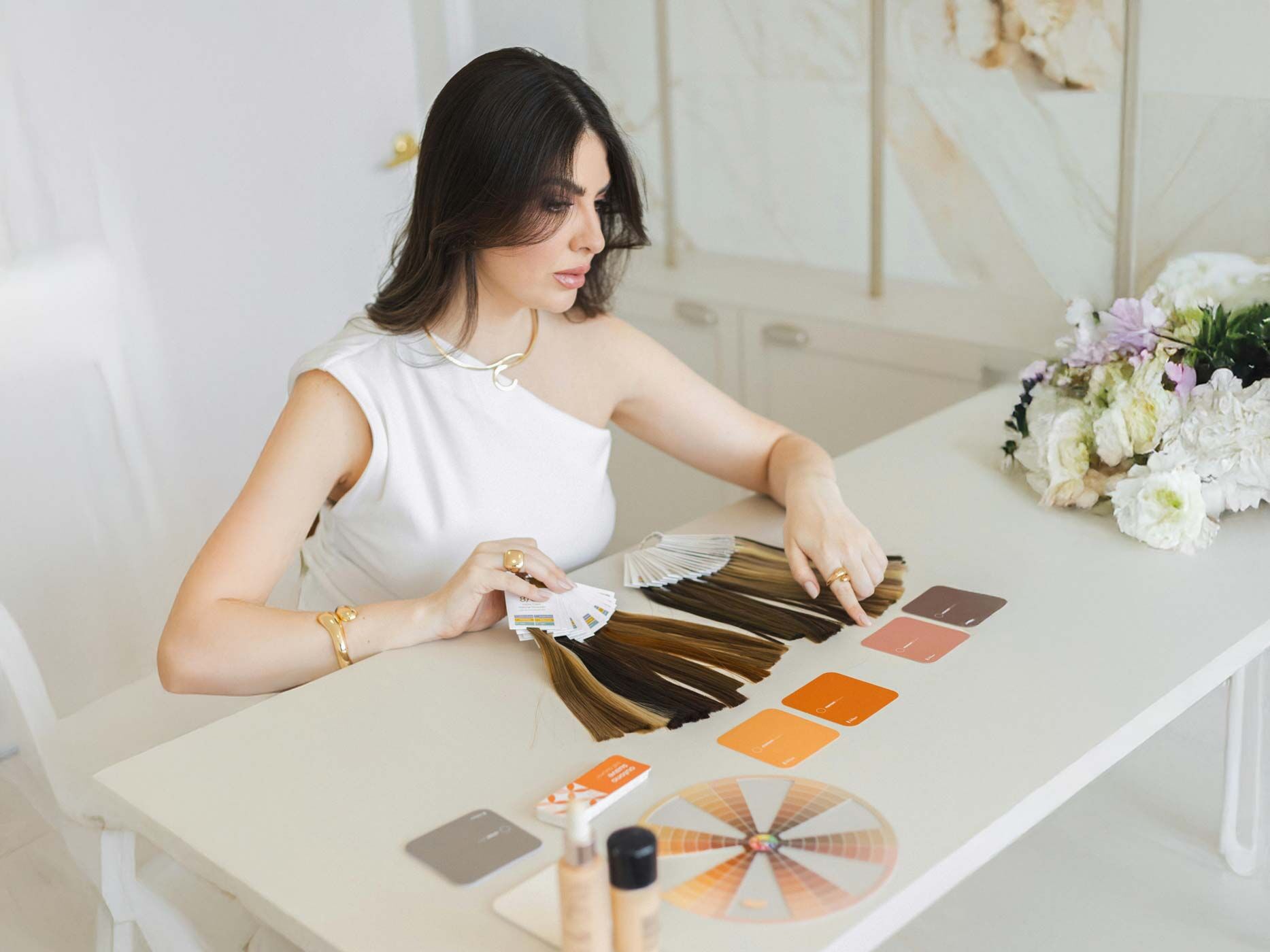 Eine Frau sitzt an einem Tisch, vor ihr sind verschiedene Haarteile und Farbbeispiele ausgebreitet.