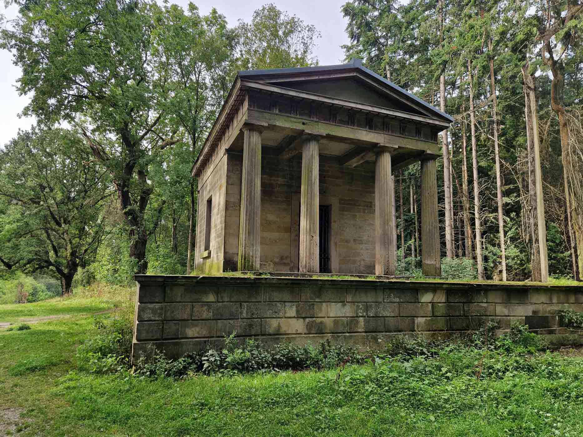 Zu sehen ist ein gebauter, alter Tempel auf einem Grasweg.