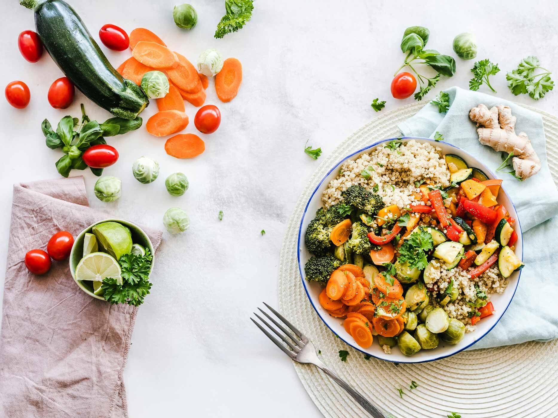 Auf dem Tisch ist viel Gemüse verteilt, in einer Schüssel ist ein Gericht mit Gemüse, Reis und Kräutern angerichtet.