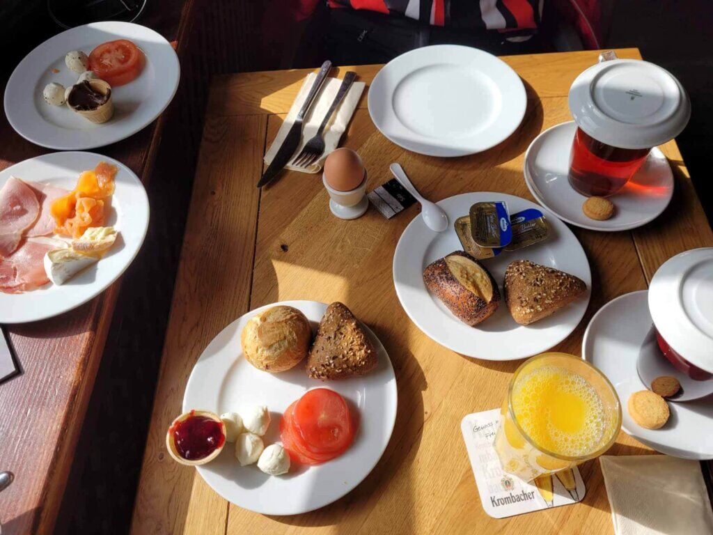 Ein Tisch gedeckt mit einem ausgewogenen Frühstück mit Brötchen, Eiern, Aufschnitt, Saft und Kaffee.