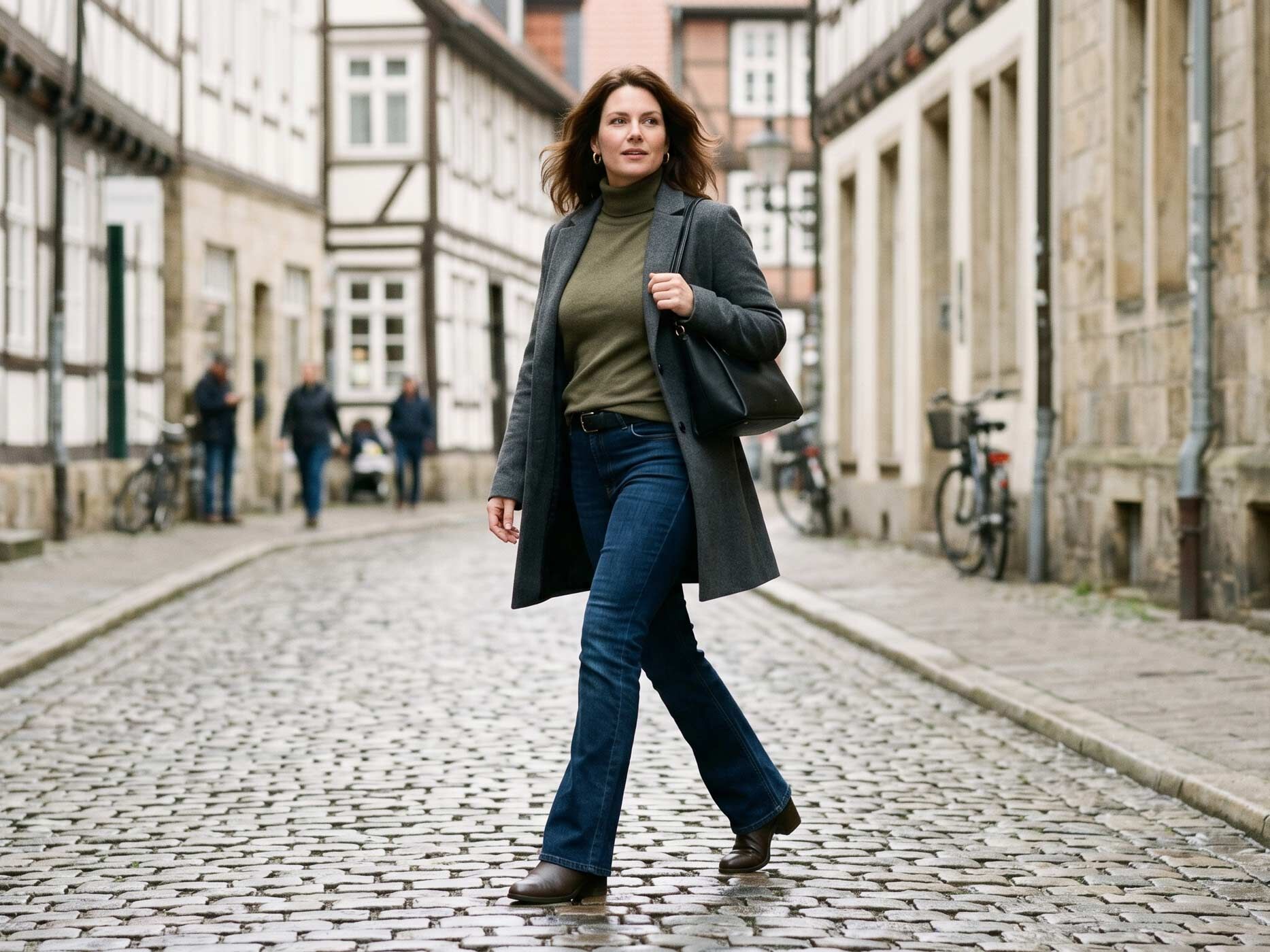 Eine Frau mit leicht rundlicher Körpermitte trägt eine dunkle Bootcut-Jeans, einen Rollkragenpullover und einen langen Mantel. Der ausgestellte Beinverlauf sorgt für ausgewogene Proportionen und eine harmonische Silhouette.