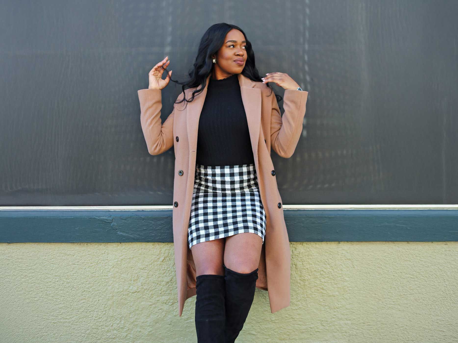 Eine Frau mit kariertem Rock lehnt an einer Wand.