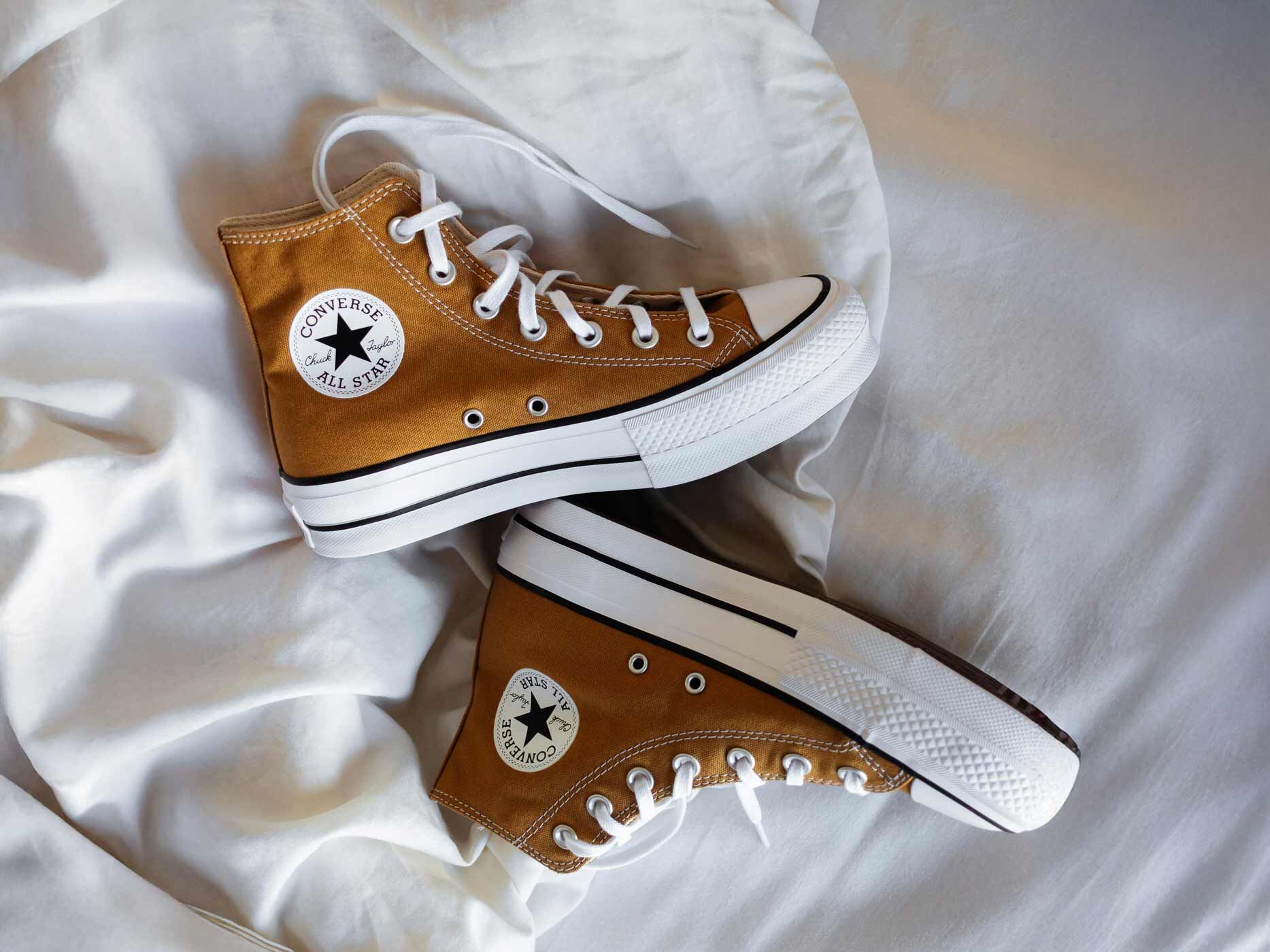 Auf einer weißen Decke liegt ein Paar hohe, braune Chucks.