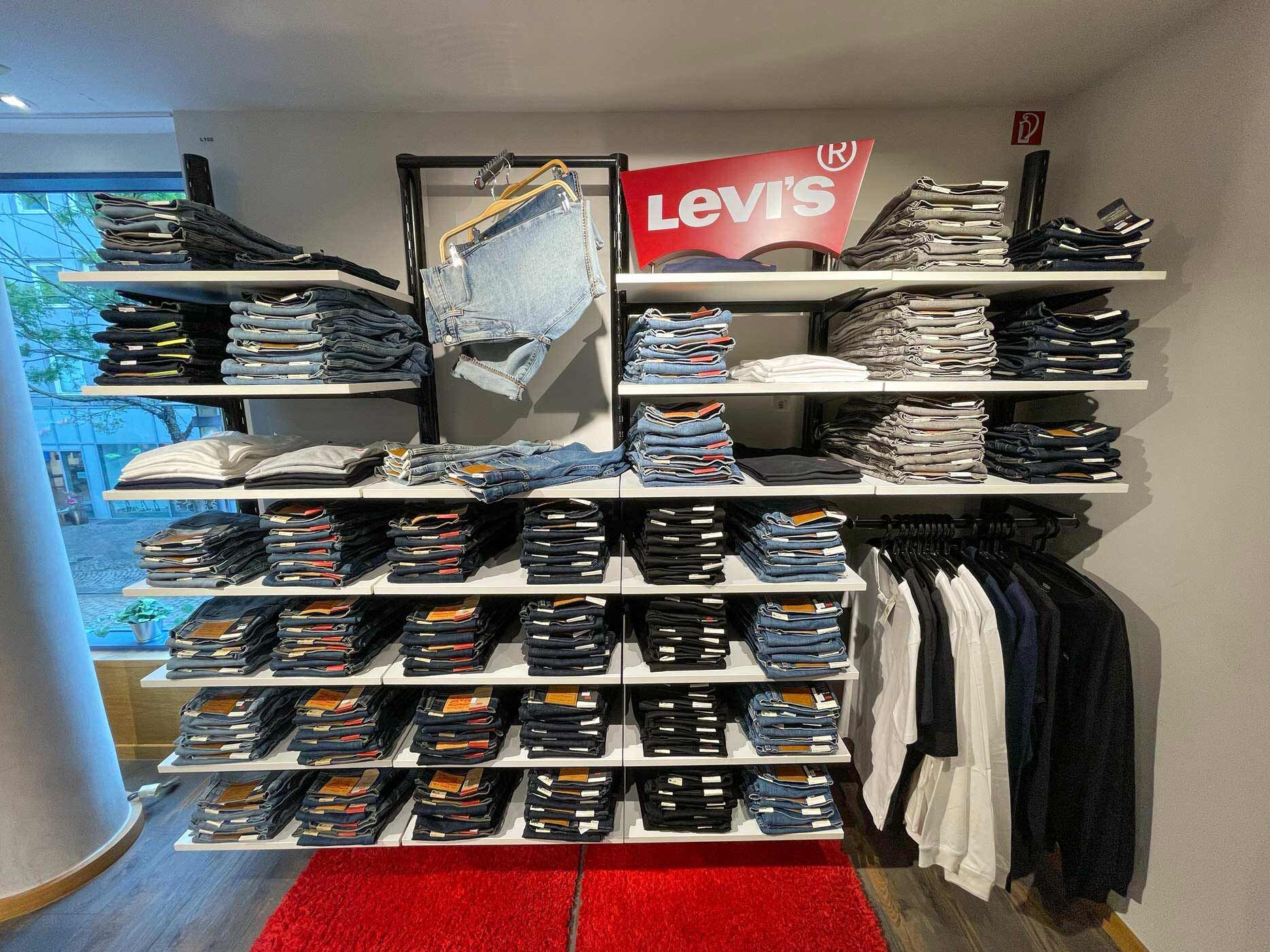 Präsentation verschiedener Levi's Herrenjeans in einem Modegeschäft. Gefaltete Jeans in unterschiedlichen Farben und Waschungen sind übersichtlich in Regalen und auf Ablageflächen angeordnet.