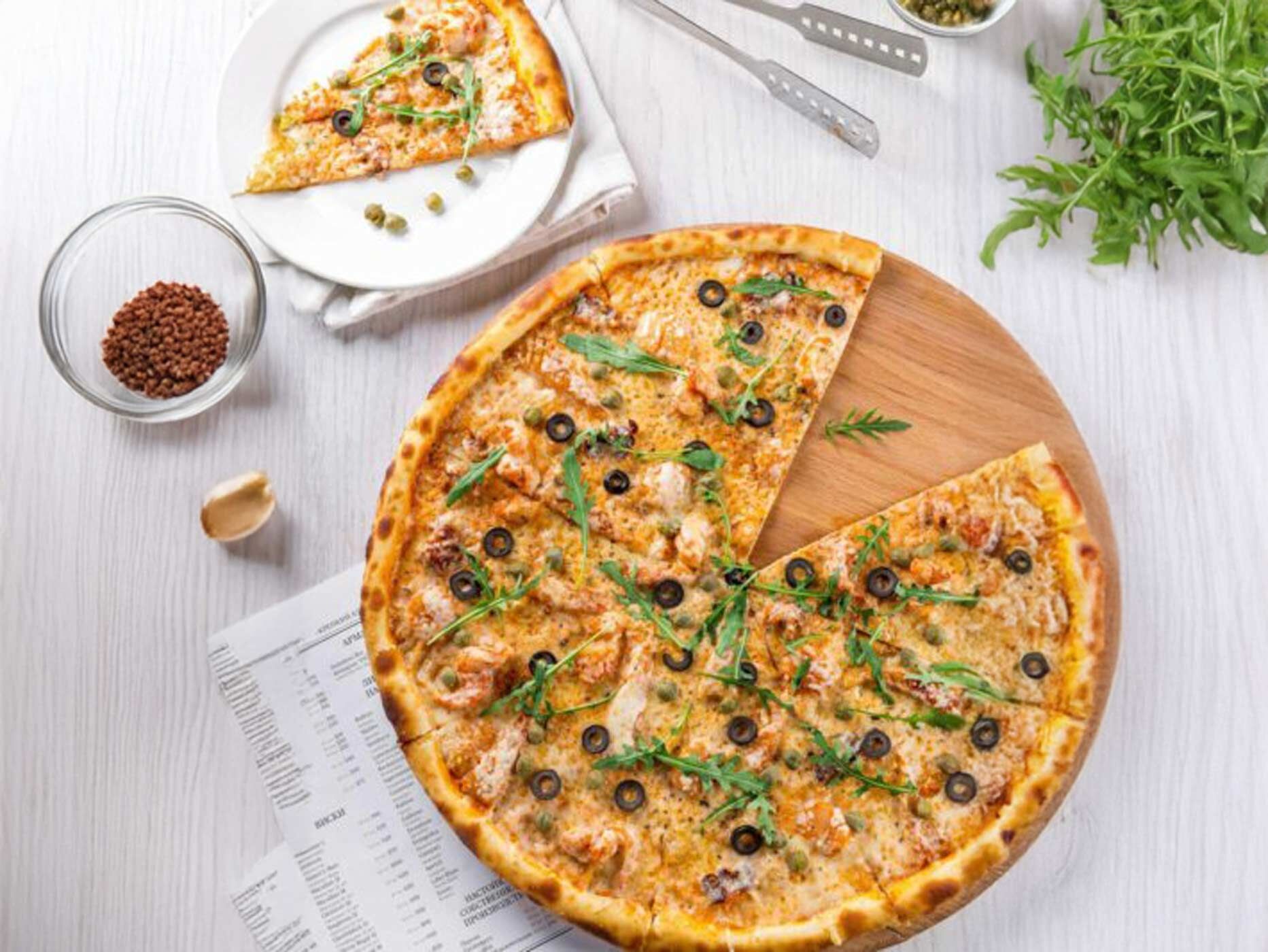 Eine Pizza mit Oliven und Rucola steht auf einem Tisch. 