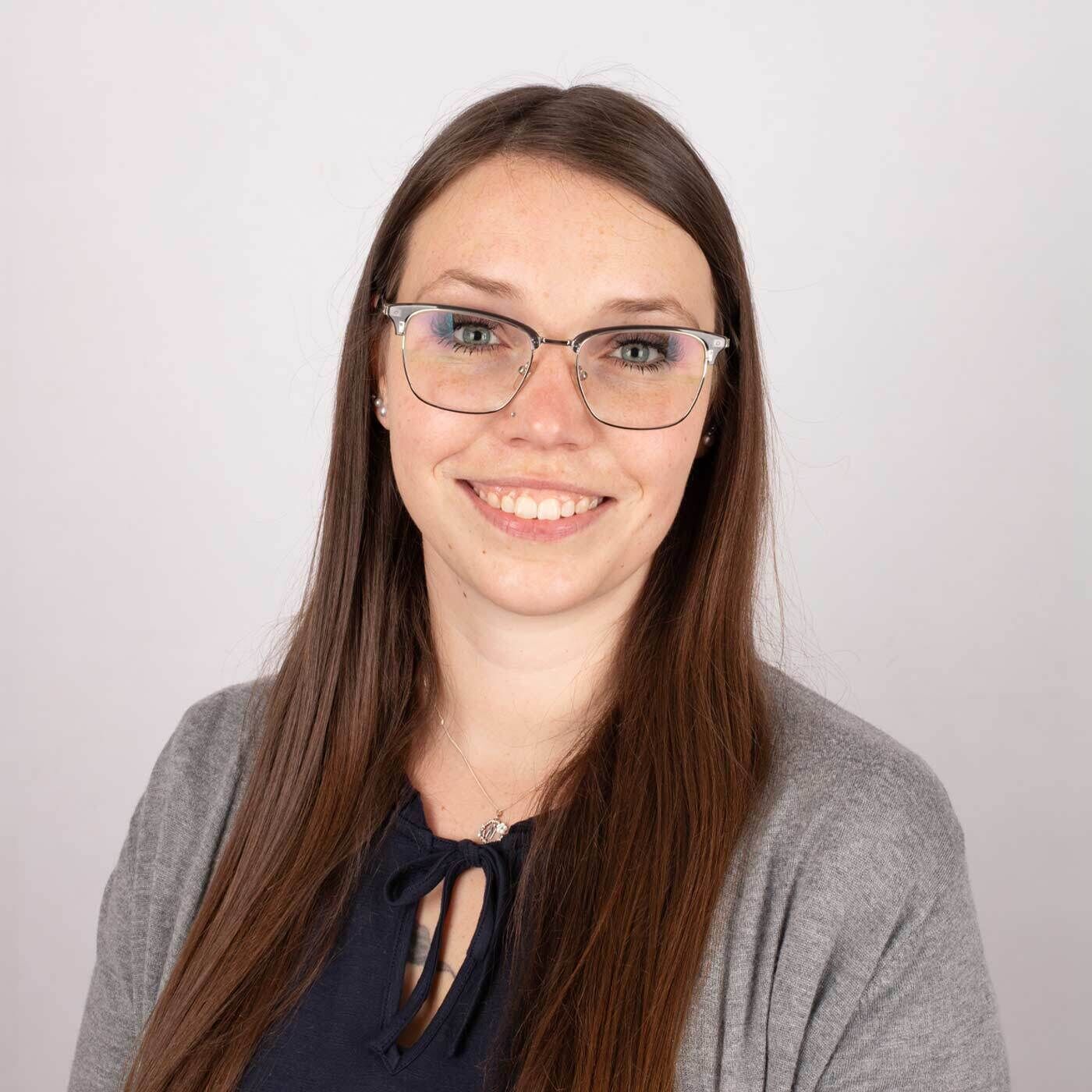 Portraitfoto von Senoritas ICON-Expertin Jana. Sie tr&auml;gt eine Brille, ein schwarzes T-Shirt mit grauer Jacke und hat lange brauen Haare. 