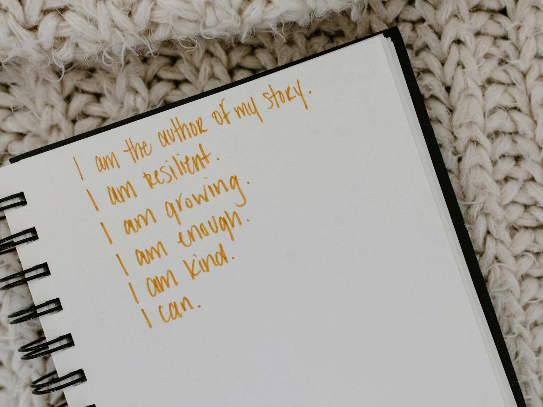 In einem Bullet Journal stehen verschiedene Sätze zur Selbstbestärkung, geschrieben mit einem gelben Stift.