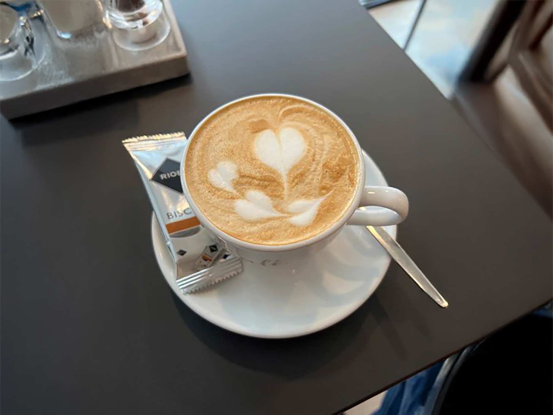 Eine Tasse Kaffee steht auf einer Untertasse, daneben liegt ein Keks.