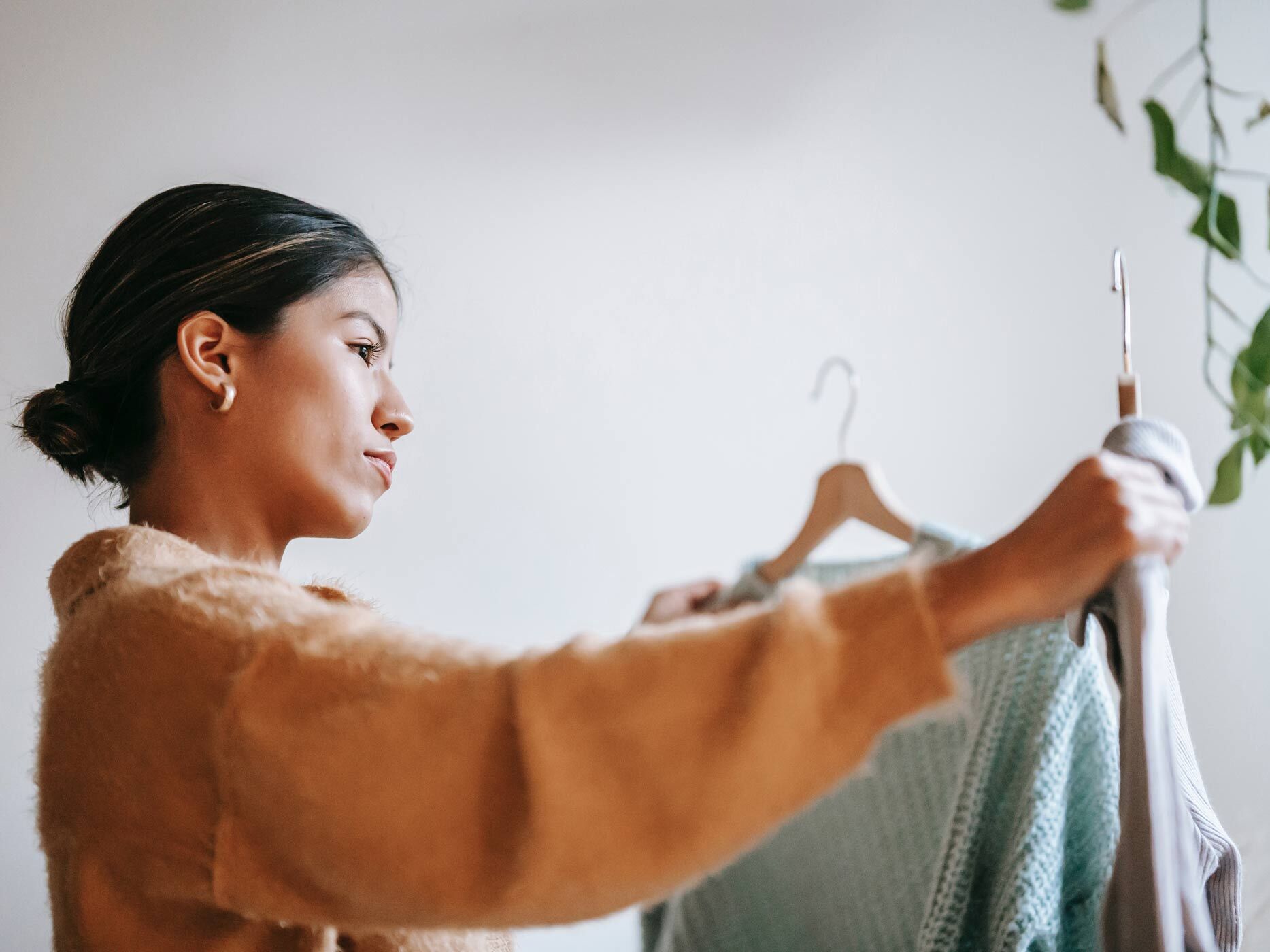 Frau hält ein Kleidungsstück auf einem Bügel prüfend hoch