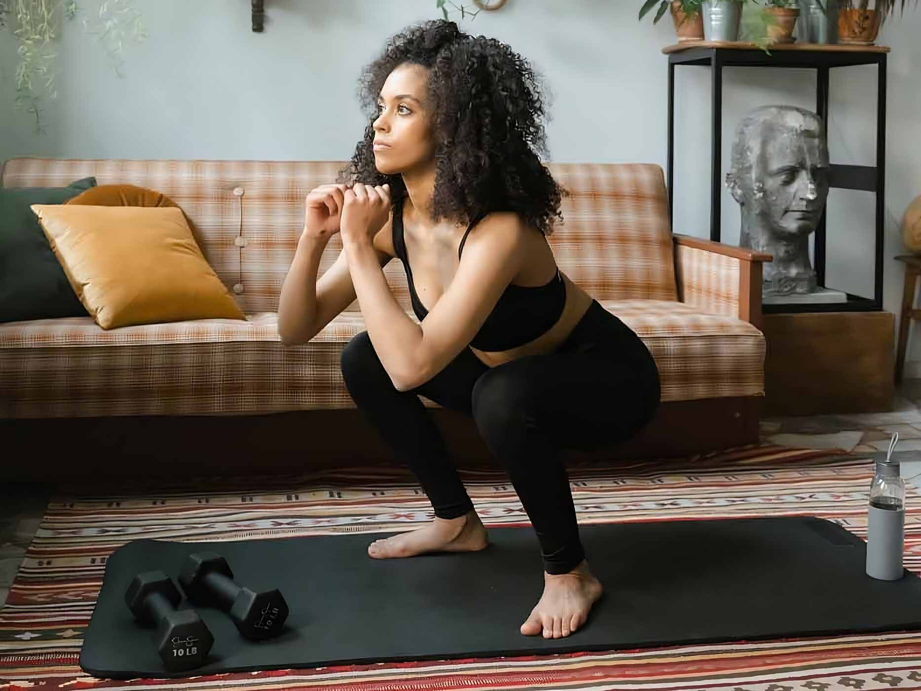 Frau im Sportdress macht Squats in ihrem Wohnzimmer
