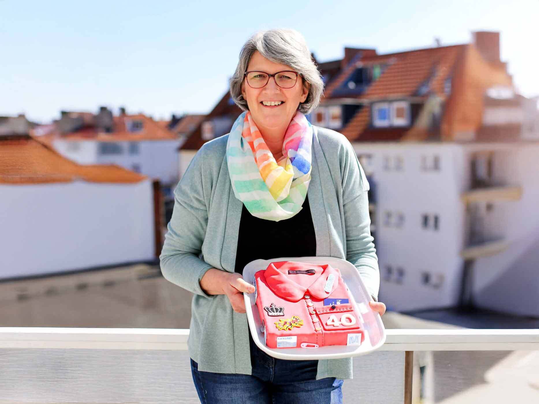 Mitarbeiterin Gabriele Quittau hält eine Torte mit einem Motiv passend zu ihrem Jubiläum in der Hand