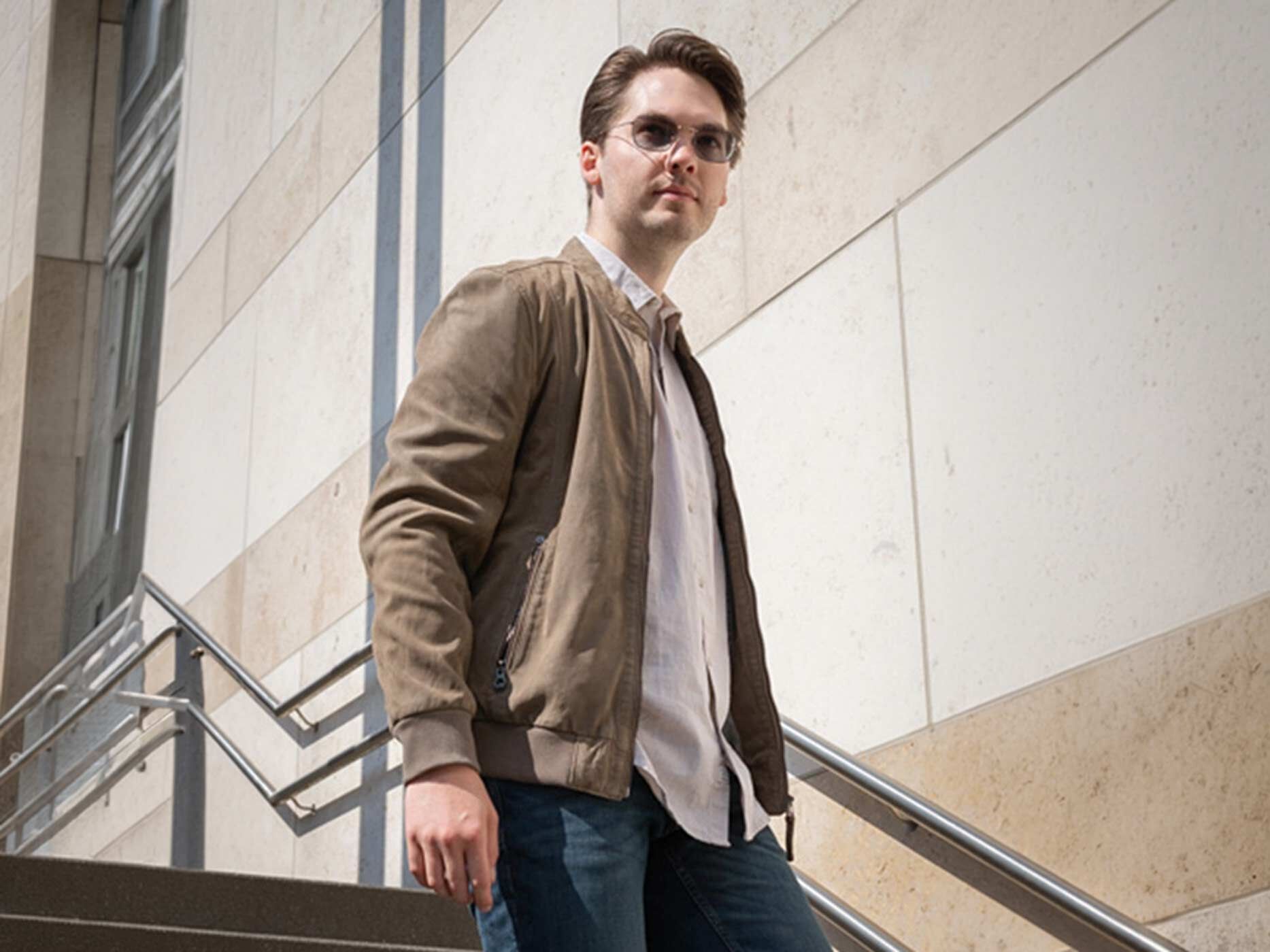Ein junger Mann in Lederjacke und Sonnenbrille geht eine Außentreppe von einem Gebäude hinunter