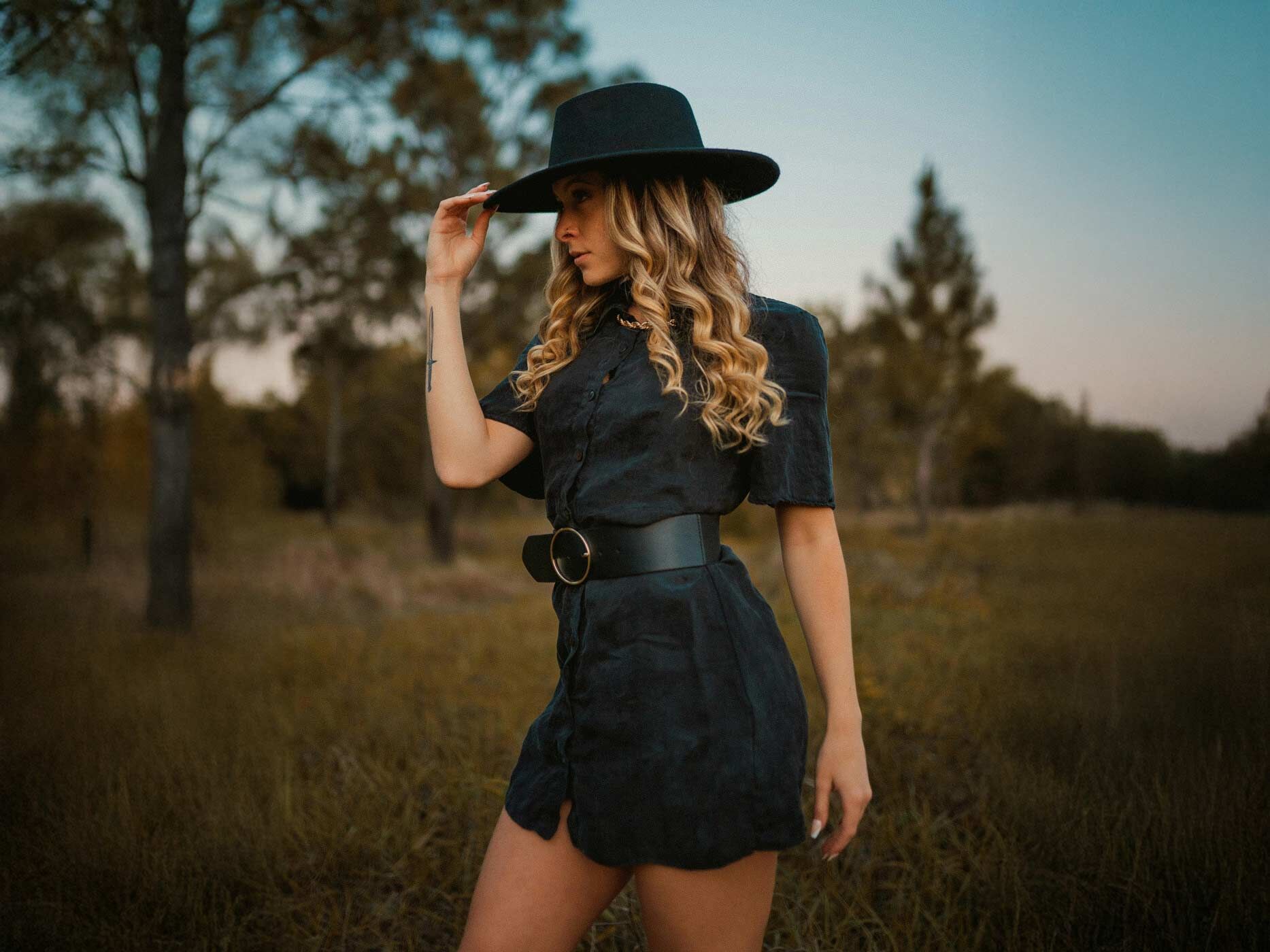 Eine Frau trägt ein kurzes schwarzes Kleid, dazu einen breiten schwarzen Gürtel und einen schwarzen Hut.