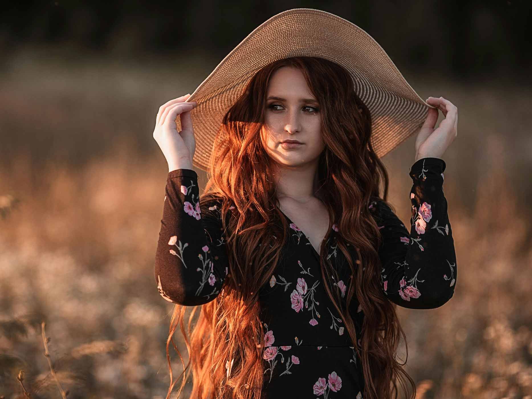 Frau trägt schwarzes Blusenkleid mit bunten Blumen und einen großen Sonnenhut vor dem Sonnenuntergang