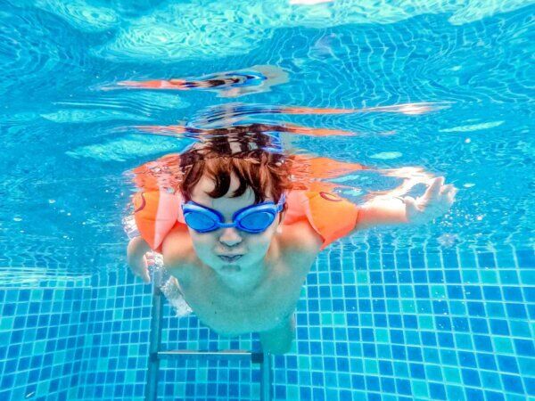 Ein Kind schwimmt mit Taucherbrille und Schwimmflügeln im Becken.
