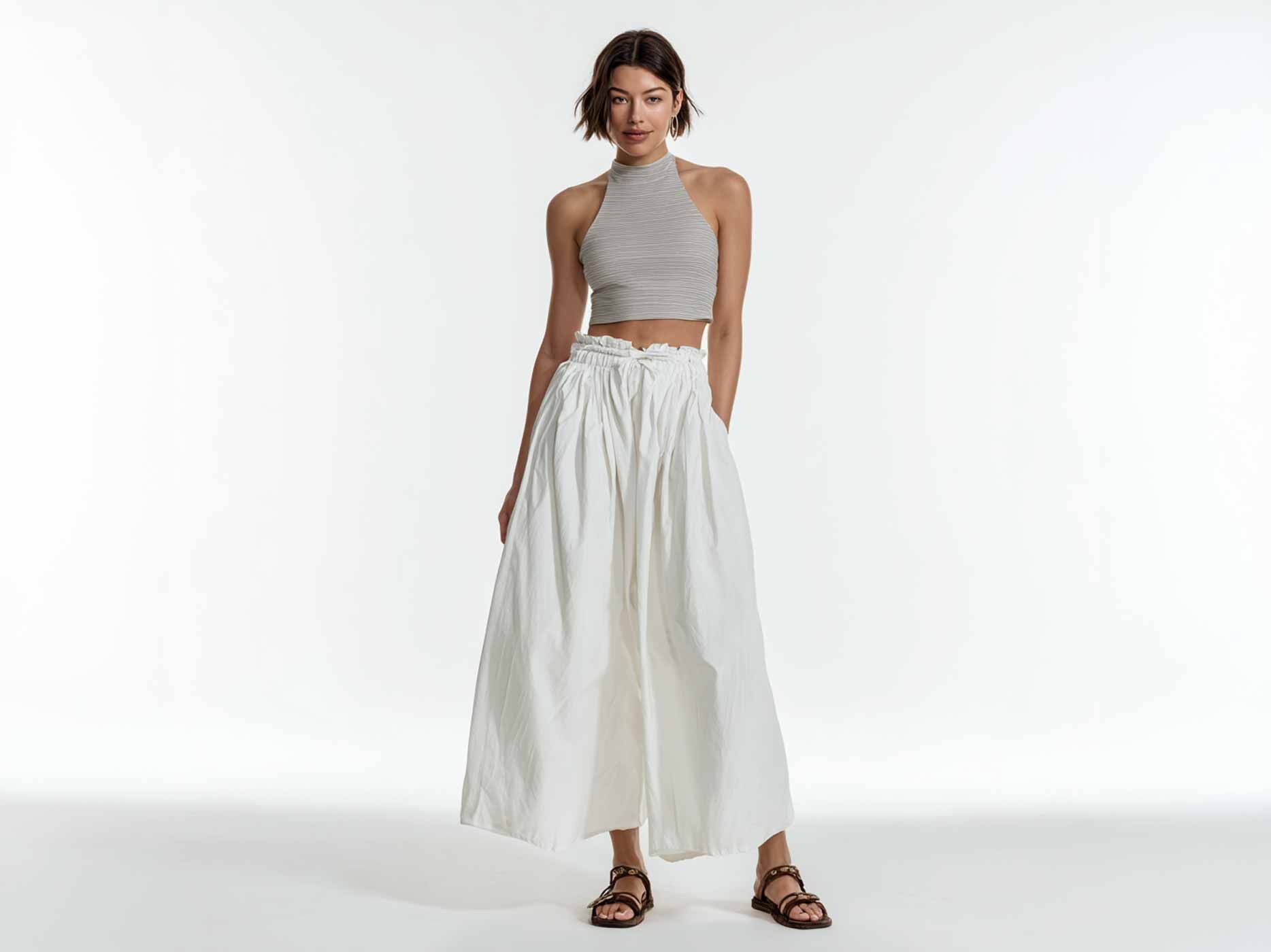 Eine Frau tr&auml;gt einen langen, weit und leicht fallenden wei&szlig;en Rock, dazu ein beiges Top und braune Sandalen.