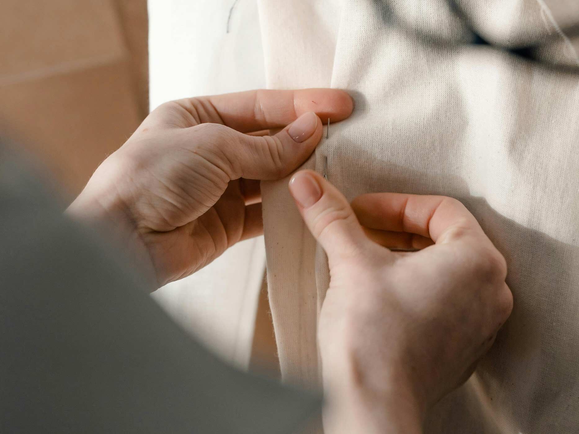 Ein heller Stoff wird mit Nadel und Faden vernäht.