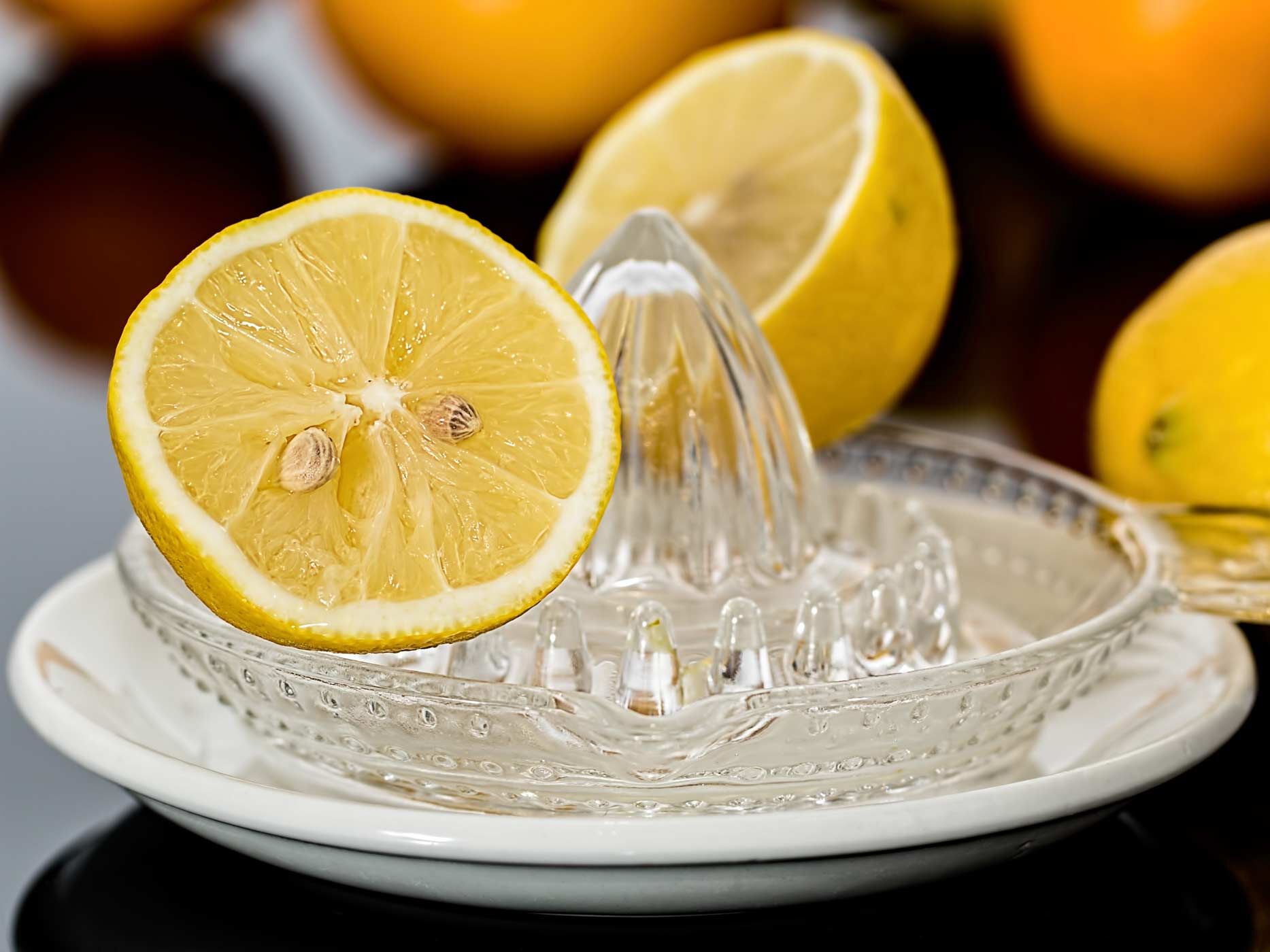 Aufgeschnittene Zitrone auf einer Glaspresse, im Hintergrund weitere Zitronen