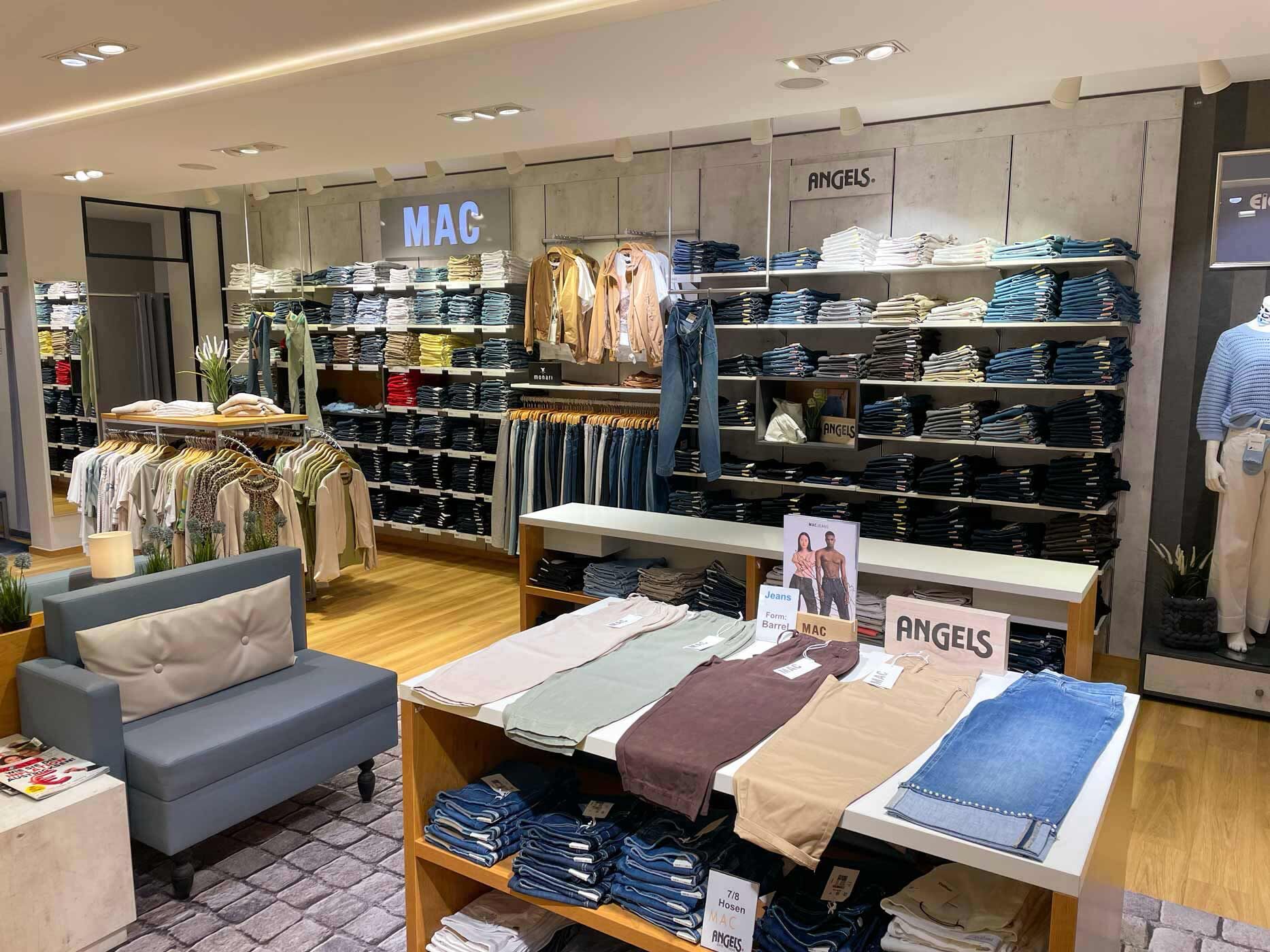 Moderne Damenjeans-Abteilung mit einer großen Auswahl an MAC und Angels Jeans. Auf Tischen und Regalen werden verschiedene Passformen, Farben und Waschungen übersichtlich präsentiert.