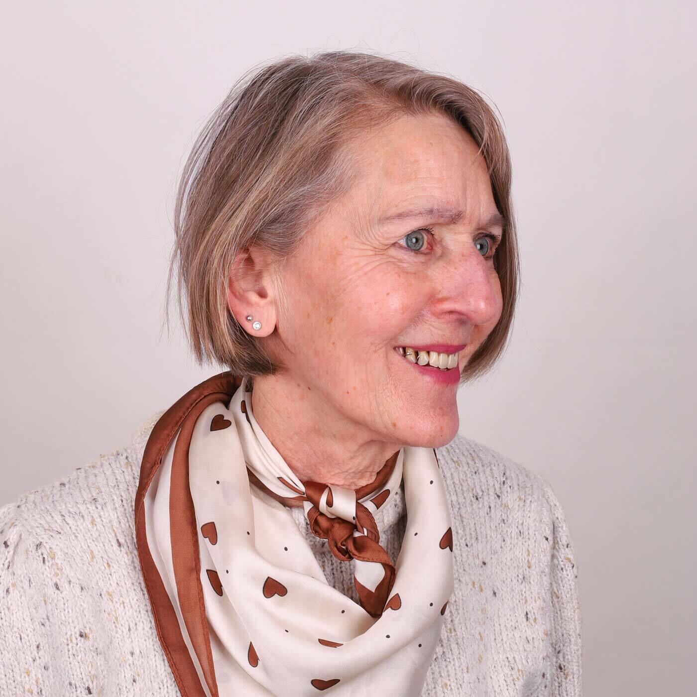Portraitfoto von Angels-Expertin Rita. Sie tr&auml;gt ihre grauen Haare als Bob und schaut zur Seite. Rita tr&auml;gt einen wei&szlig;en Pullover und ein beiges Tuch mit Herzmuster.