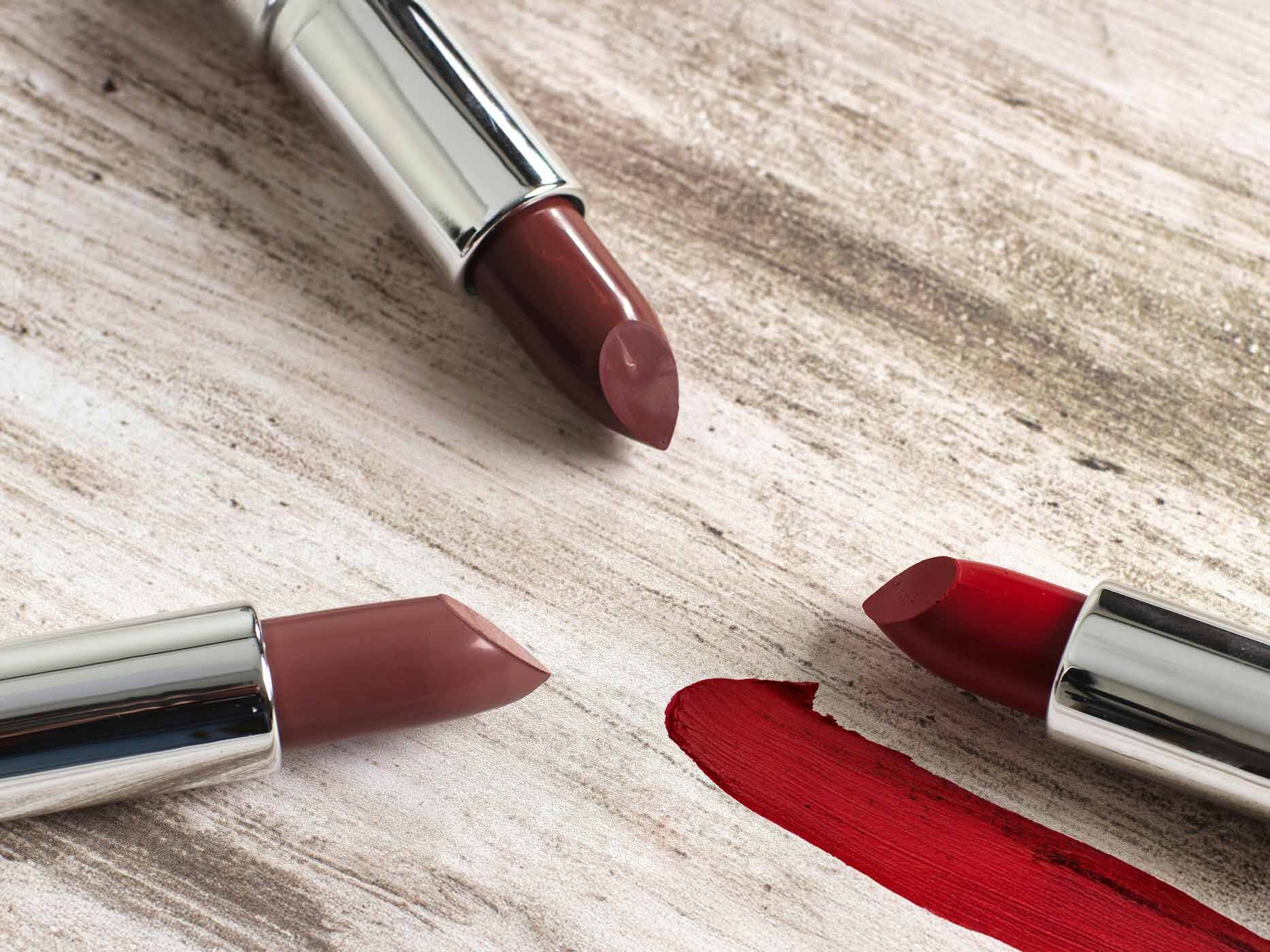 Drei ausgefahrene Lippenstifte liegen nebeneinander, zwei braune und ein roter.