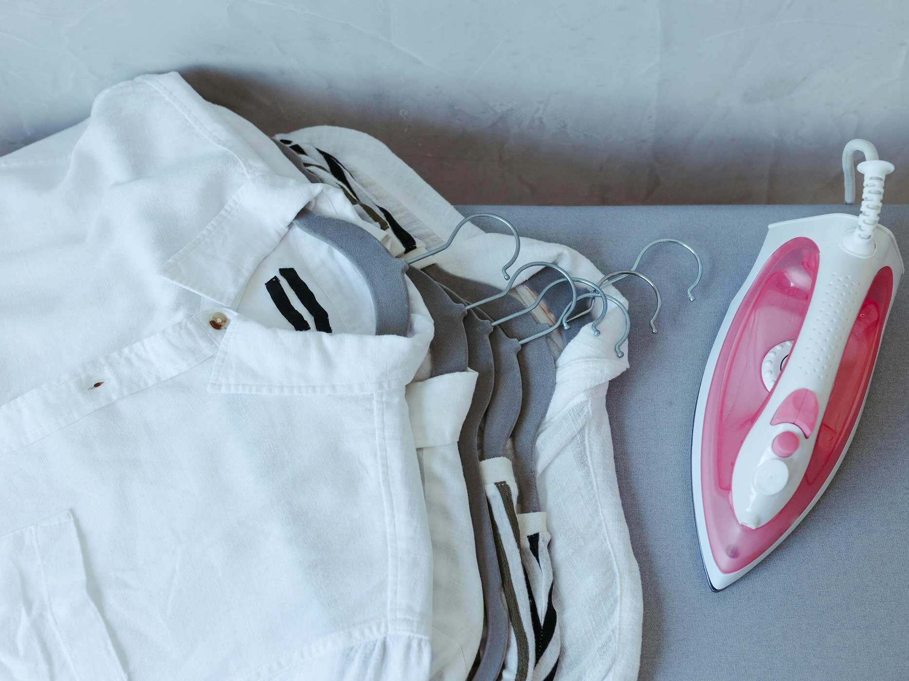 Mehrere Hemden liegen übereinander gestapelt neben einem Bügeleisen.