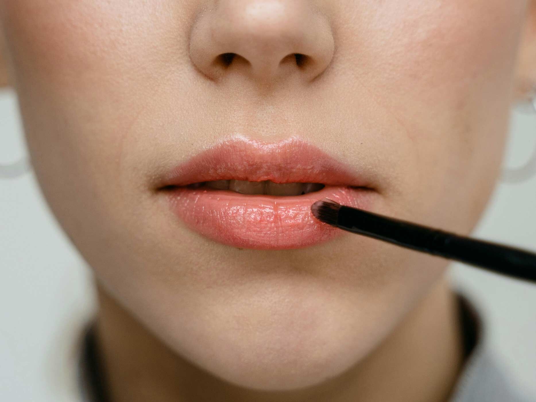 Eine Nahaufnahme, wie rosa farbener Lippenstift mit einem kleinen Pinsel auf Lippen aufgetragen wird.