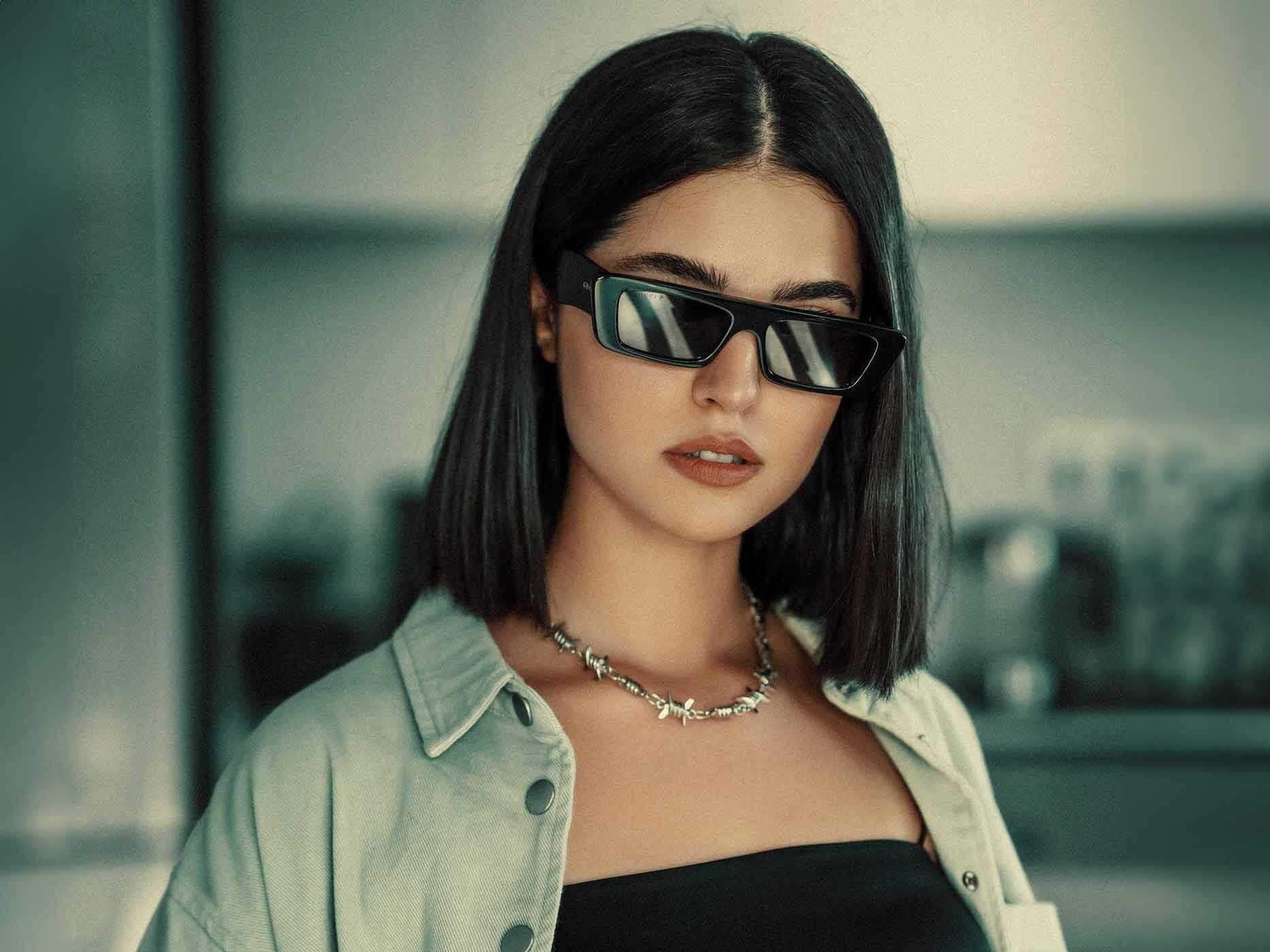 Frau trägt schwarzes, trägerloses Oberteil, dazu eine enganliegende silberne Kette und eine schwarze Sonnenbrille