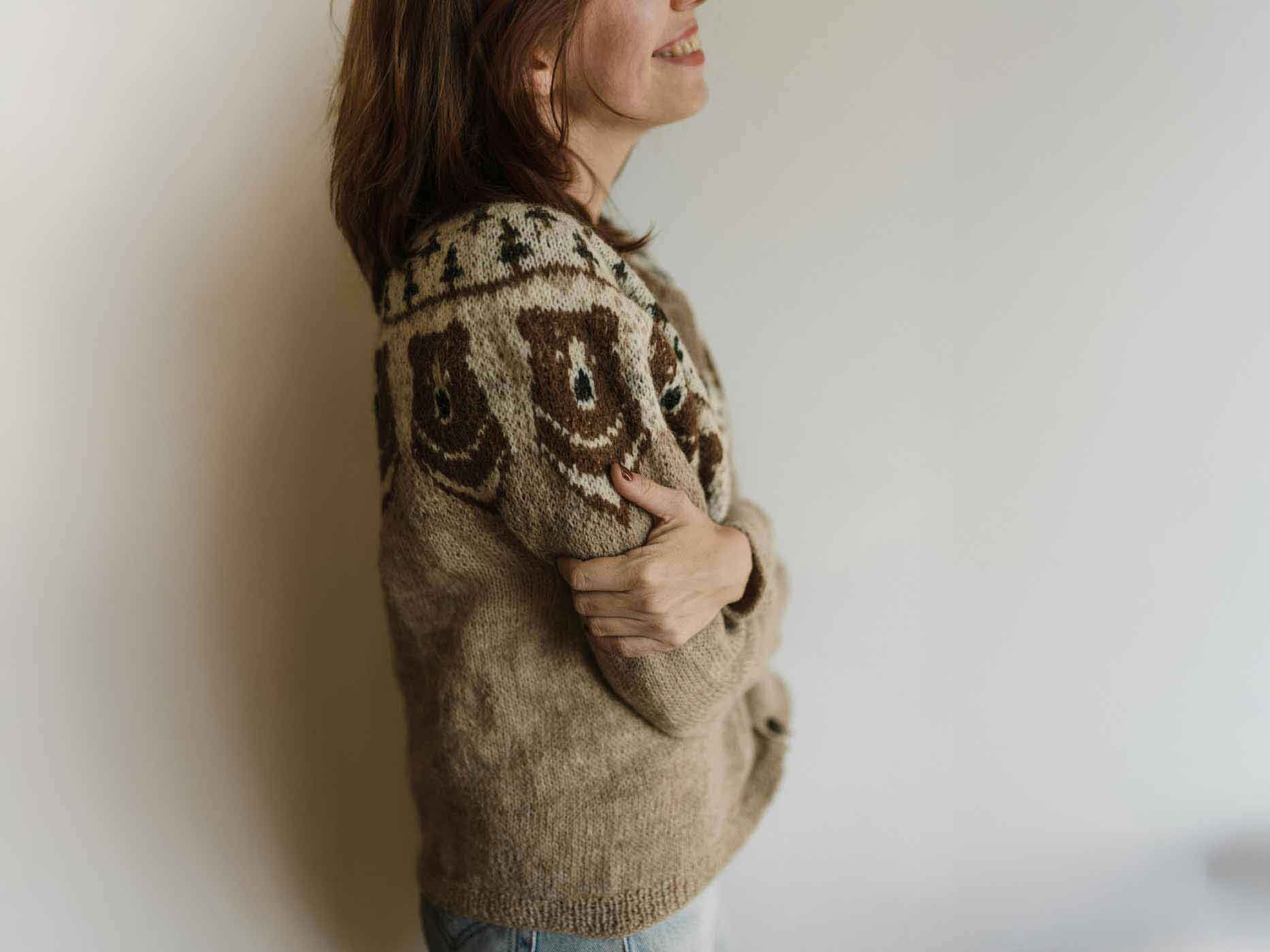 Eine Frau trägt einen braunen Wollpullover mit Muster und kuschelt sich in ihn ein.