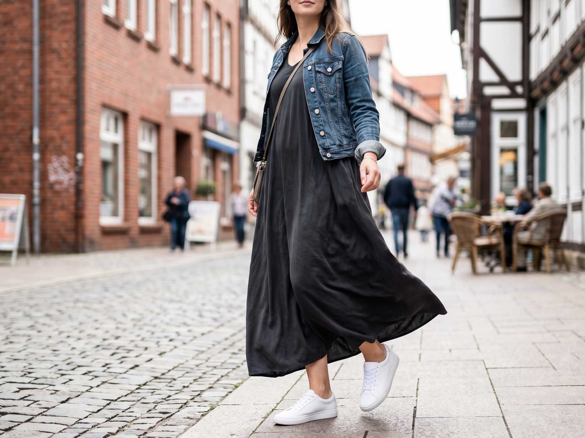 Eine Frau tr&auml;gt ein langes schwarzes Kleid mit blauer Jeansjacke und wei&szlig;en Sneakern.